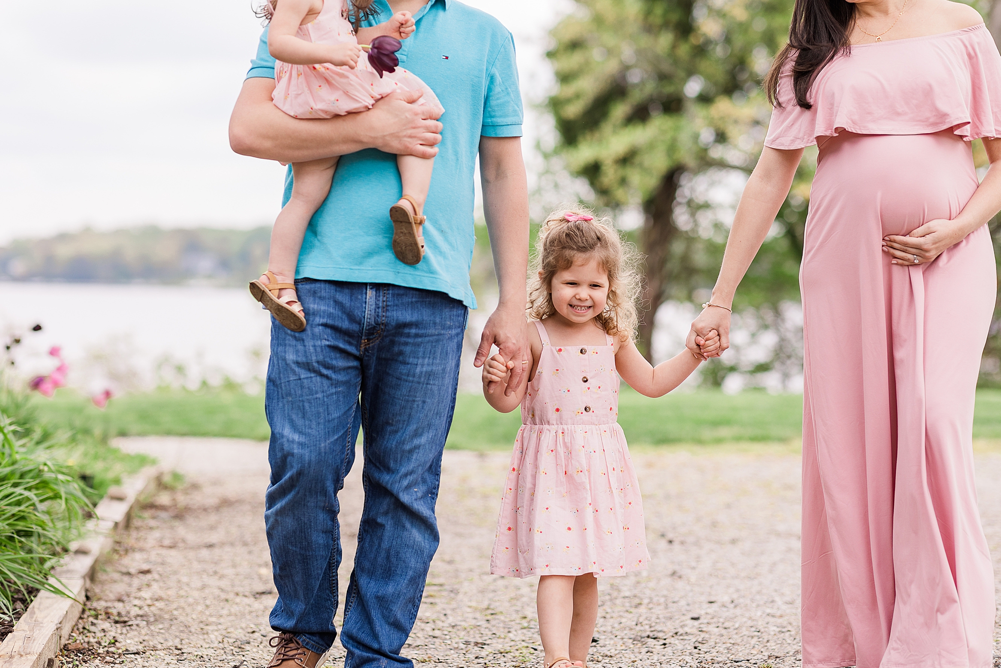 parents hold hands of daughter while dad carries younger daughter during Maternity Photos with Northern Virginia Family Photographer