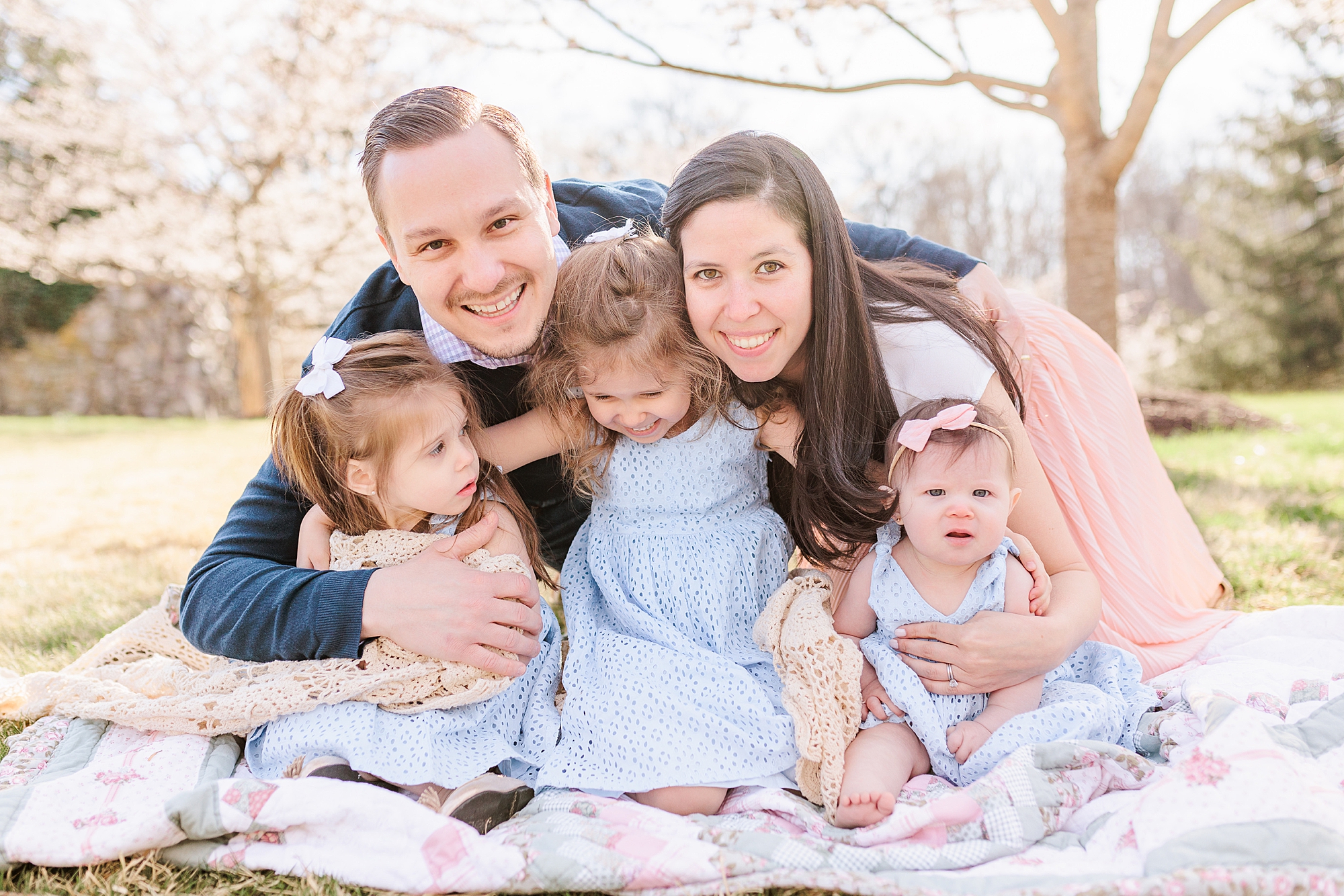 parents hug three daughters on pink and blue blanket during family photos