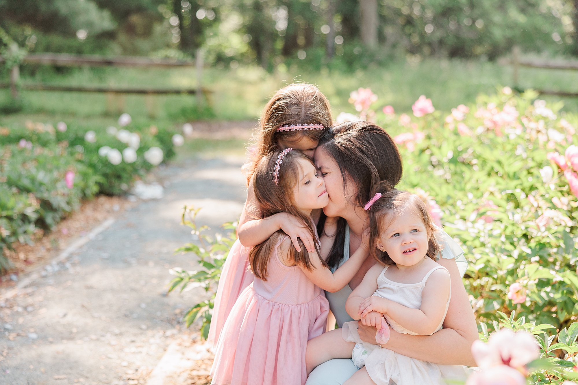 mom kisses daughter on the cheek while other daughters hug her