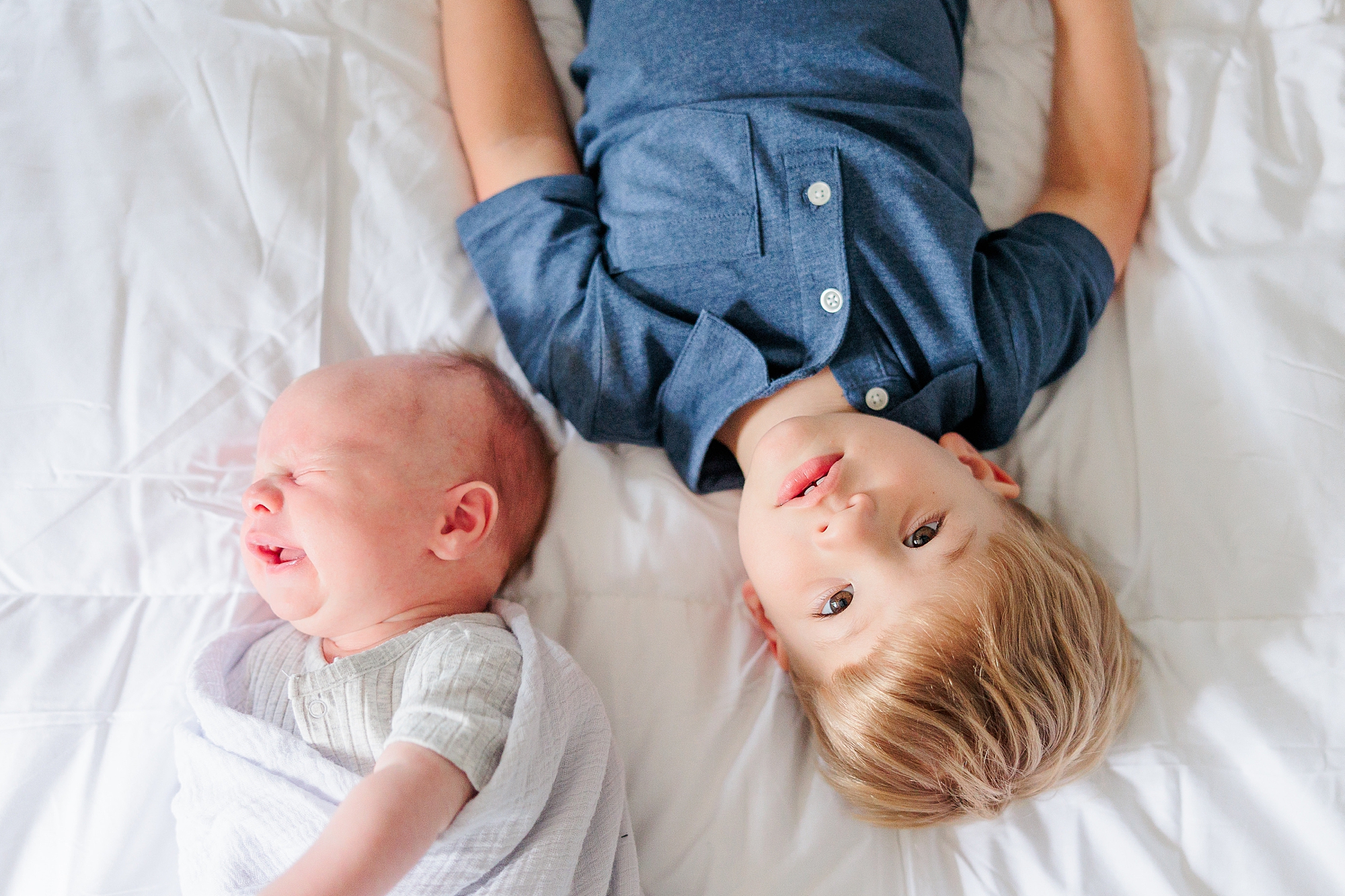 big brother lays with newborn brother on bed during lifestyle newborn photos
