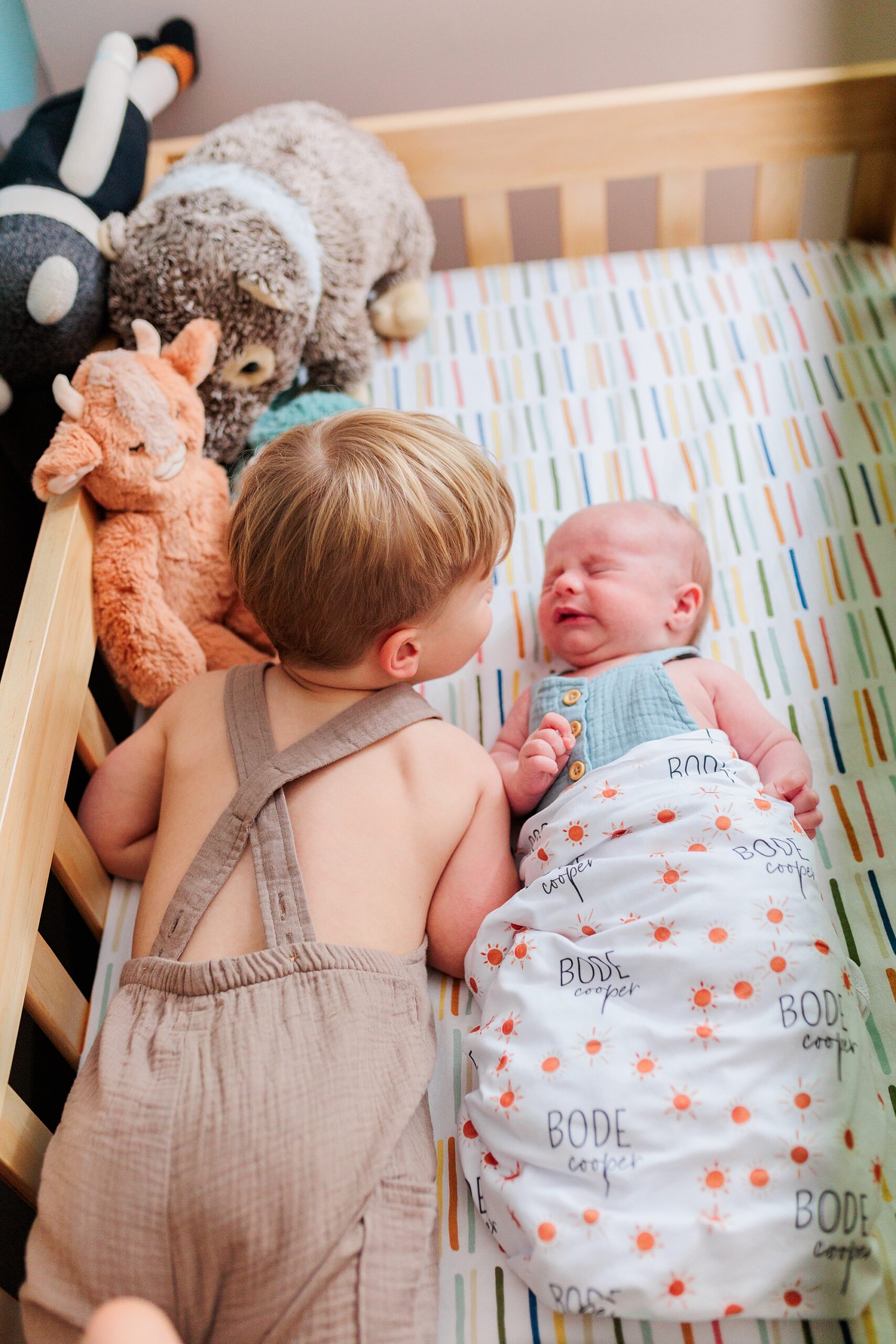 big brother lays in crib looking at sister during Maryland lifestyle newborn photos