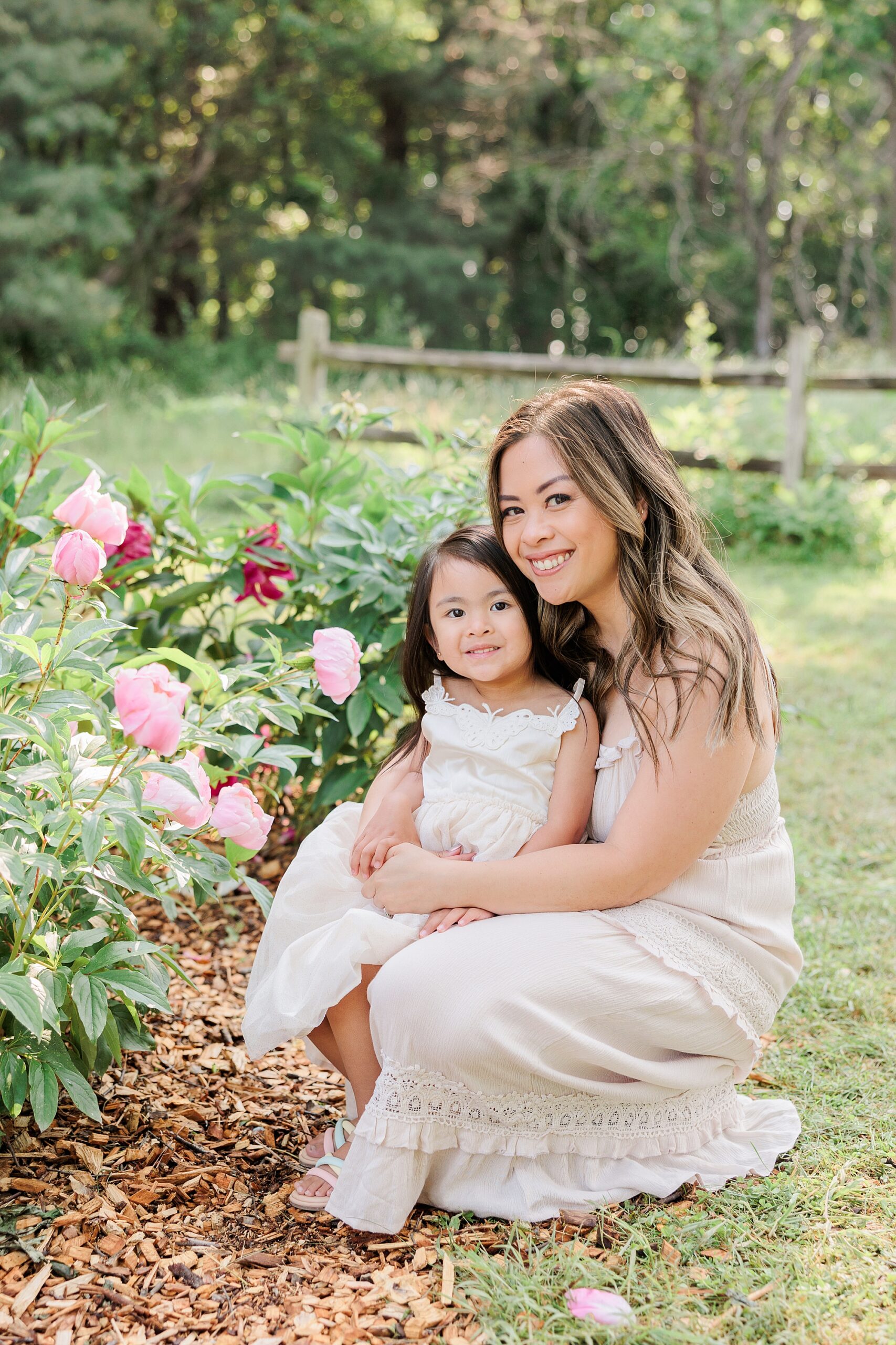 woman in pastel gown holds daughter on lap near flowers in Maryland 