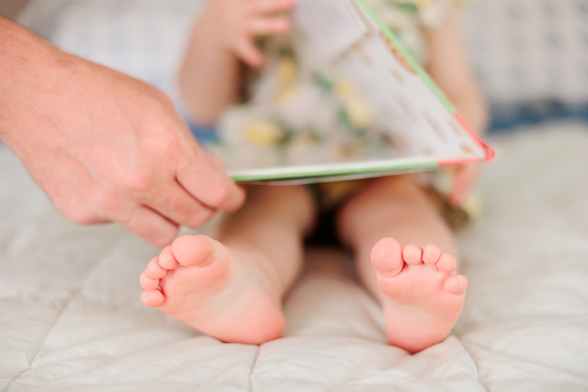 toddler's toes while she holds book on bed during lifestyle family photos in Bethesda MD