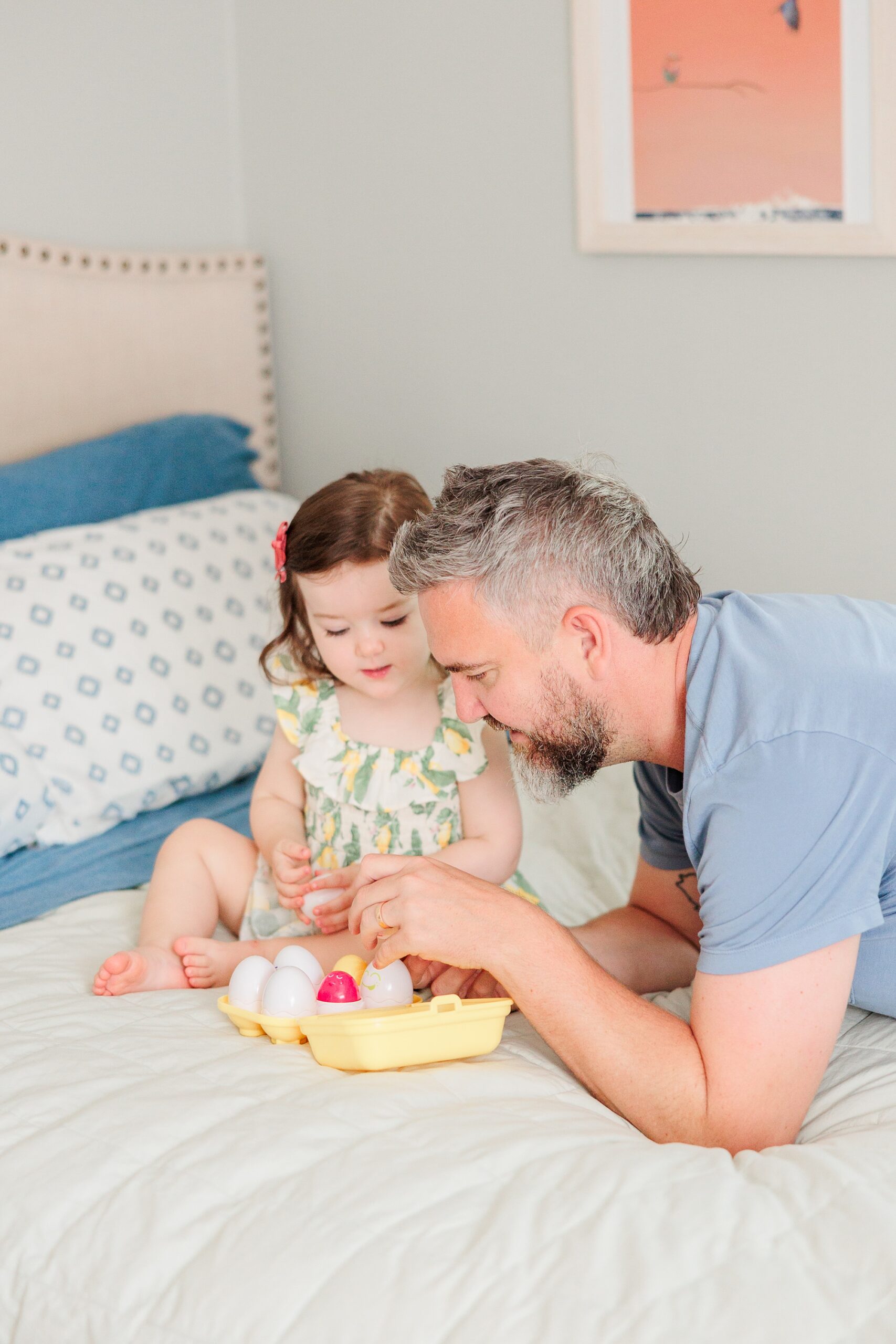 dad in blue shirt plays with daughter on bed during family photos at home