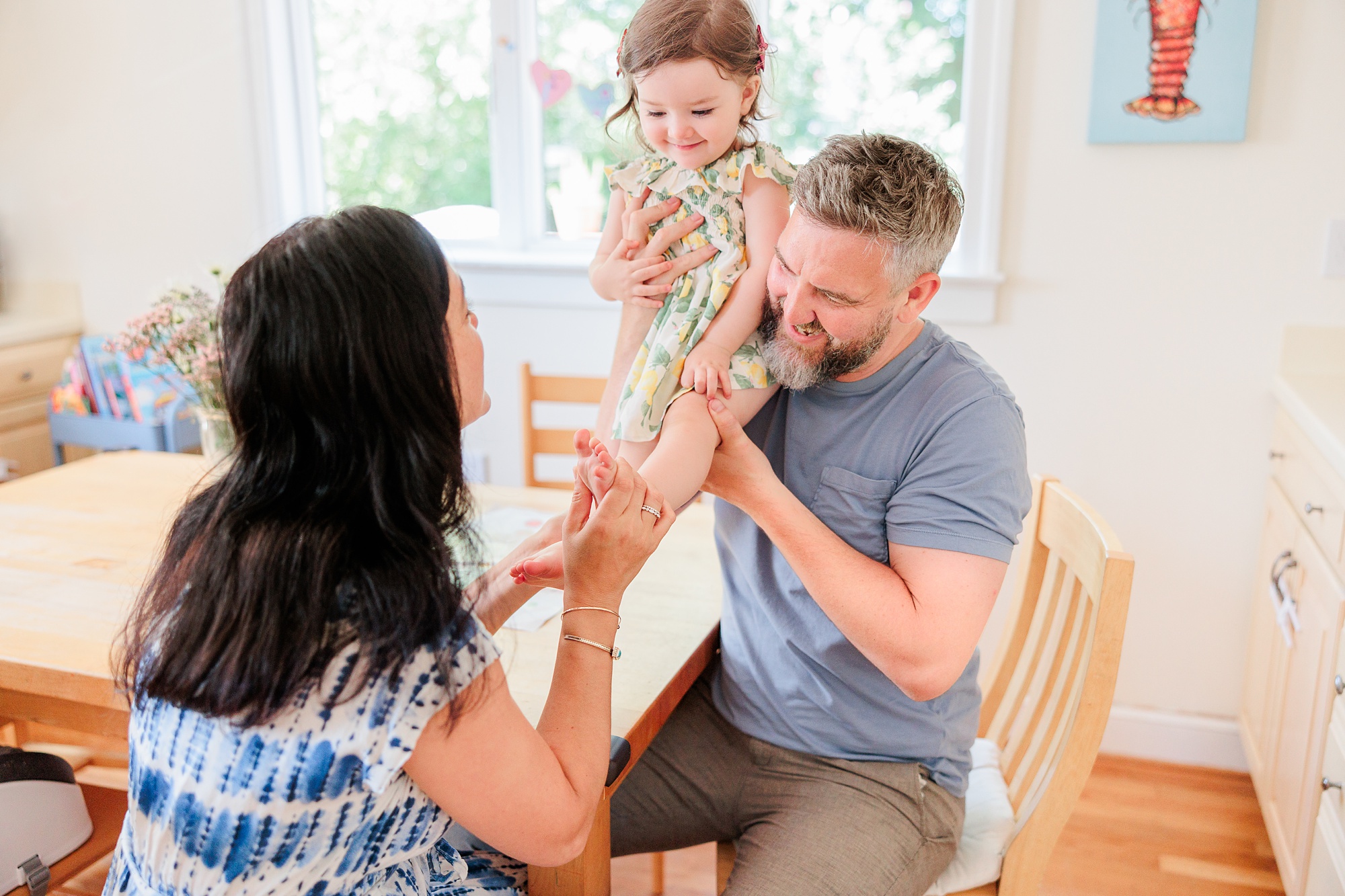 parents play with toddler next to kitchen table during lifestyle family photos in Bethesda MD