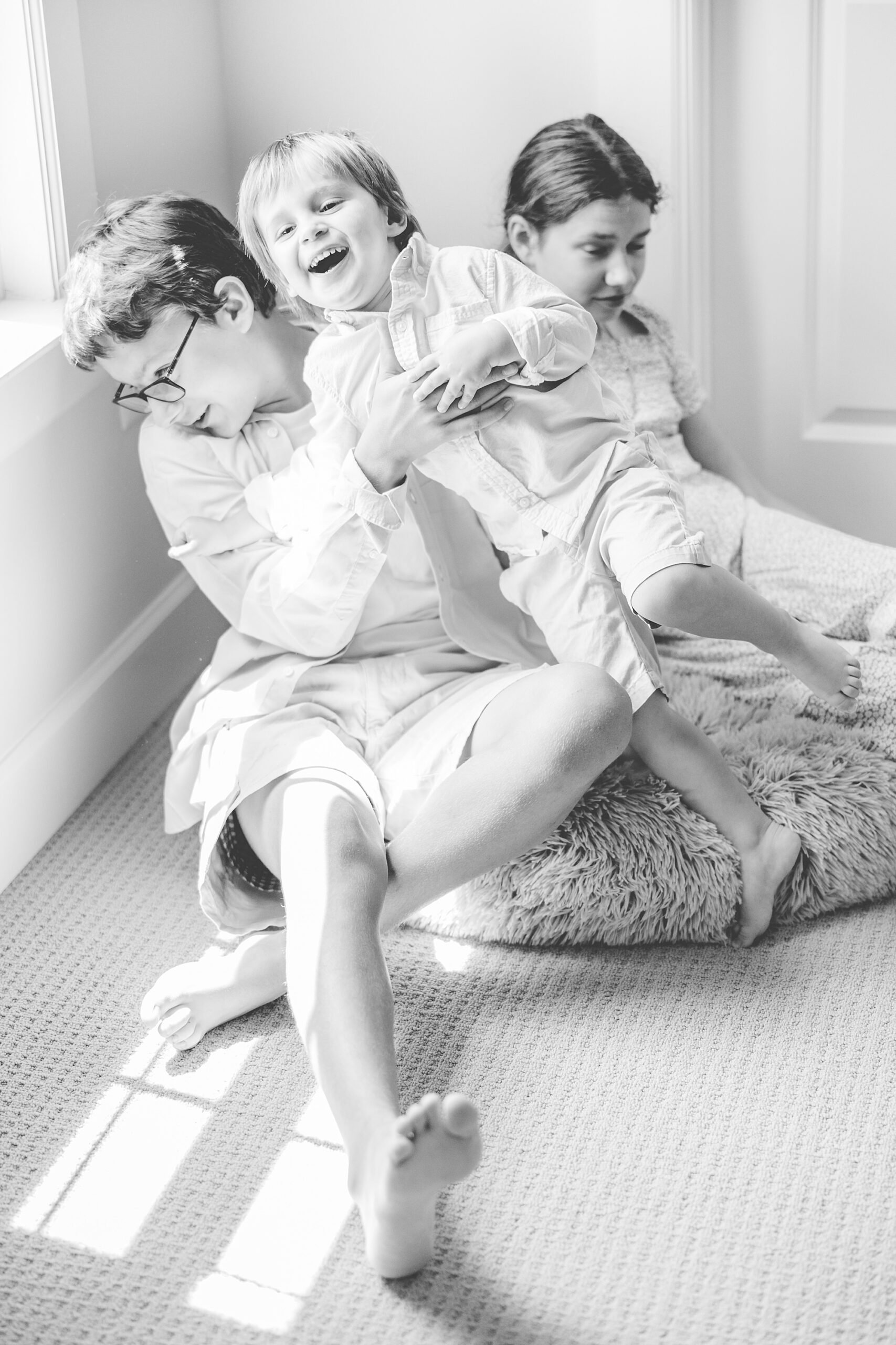 three siblings laugh together in corner of room during Maryland lifestyle family photos