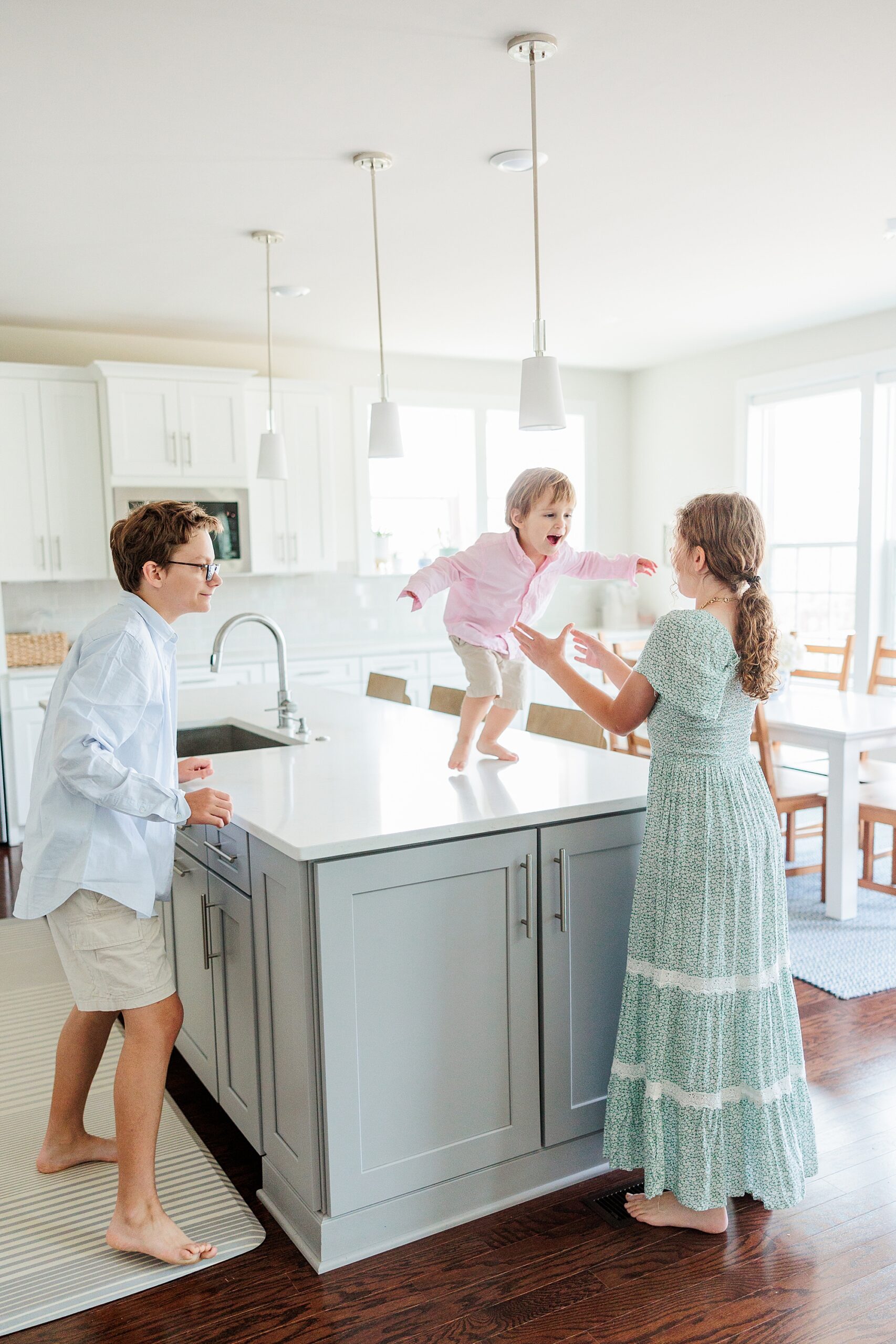 toddler stands on island in kitchen playing with siblings