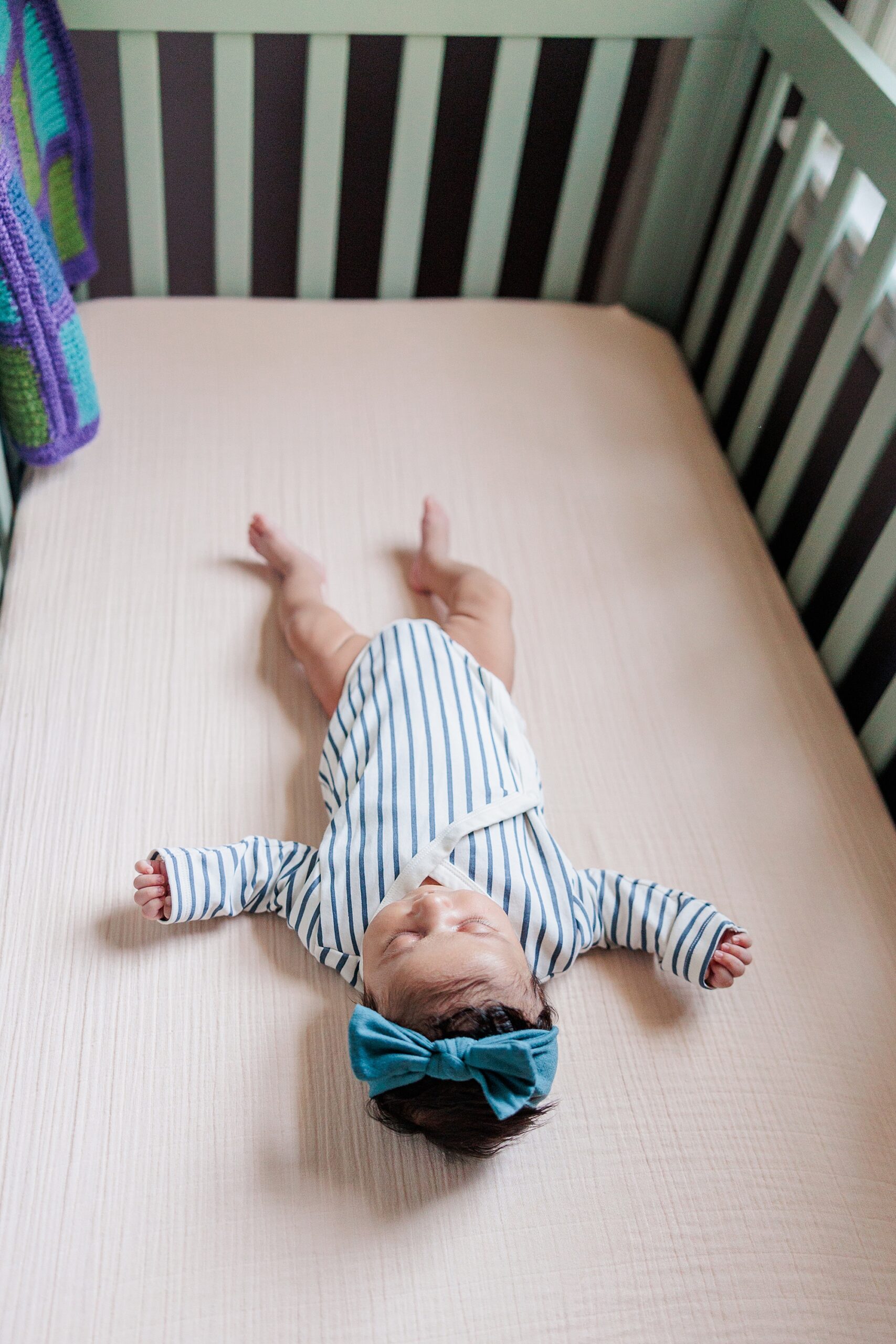 baby lays on pink sheets in blue and white striped outfits 