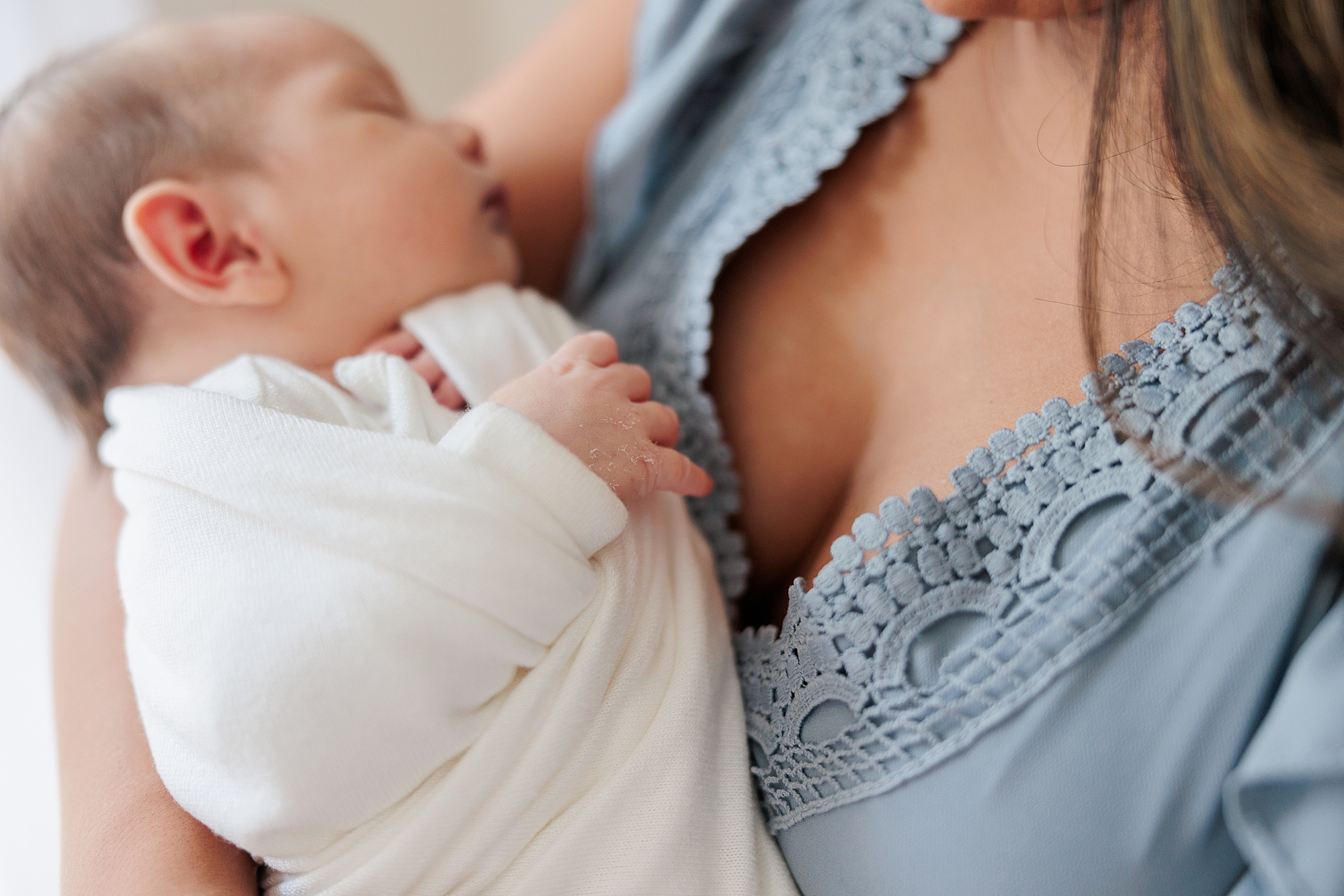 mother in blue dress holds son sleeping against her chest