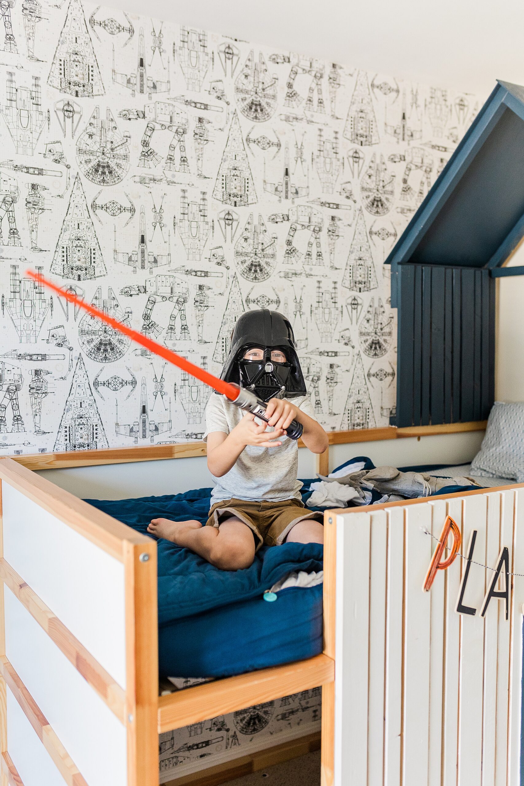toddler plays on bed with Vader mask and lightsaber