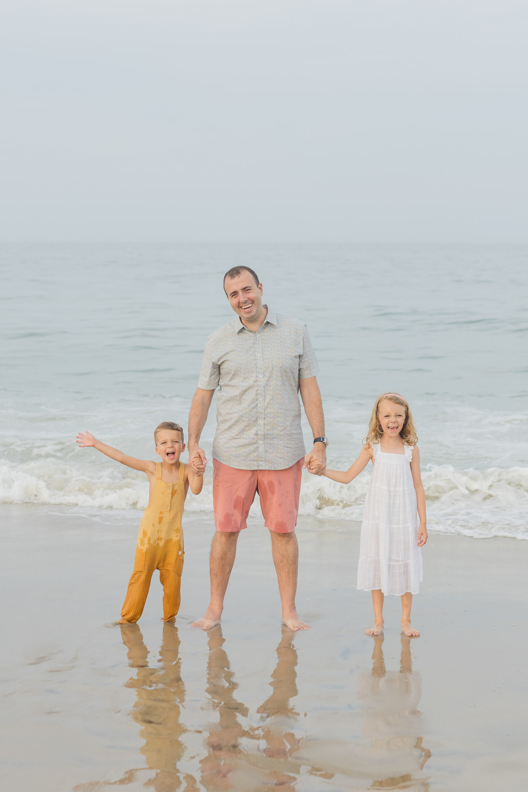 father stands on Delaware beach with two children