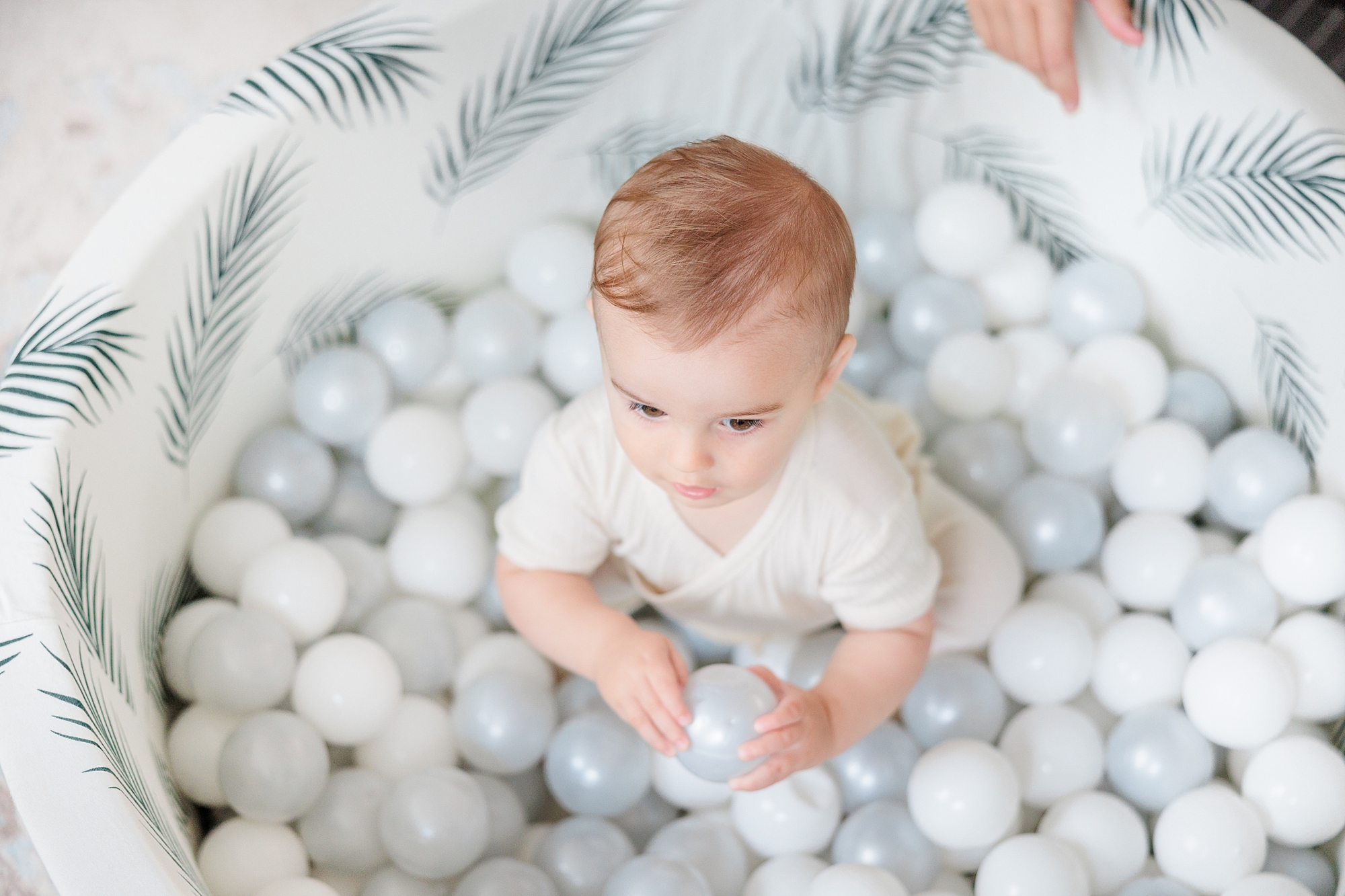 toddler plays in white and blue ball pit during family photos at home