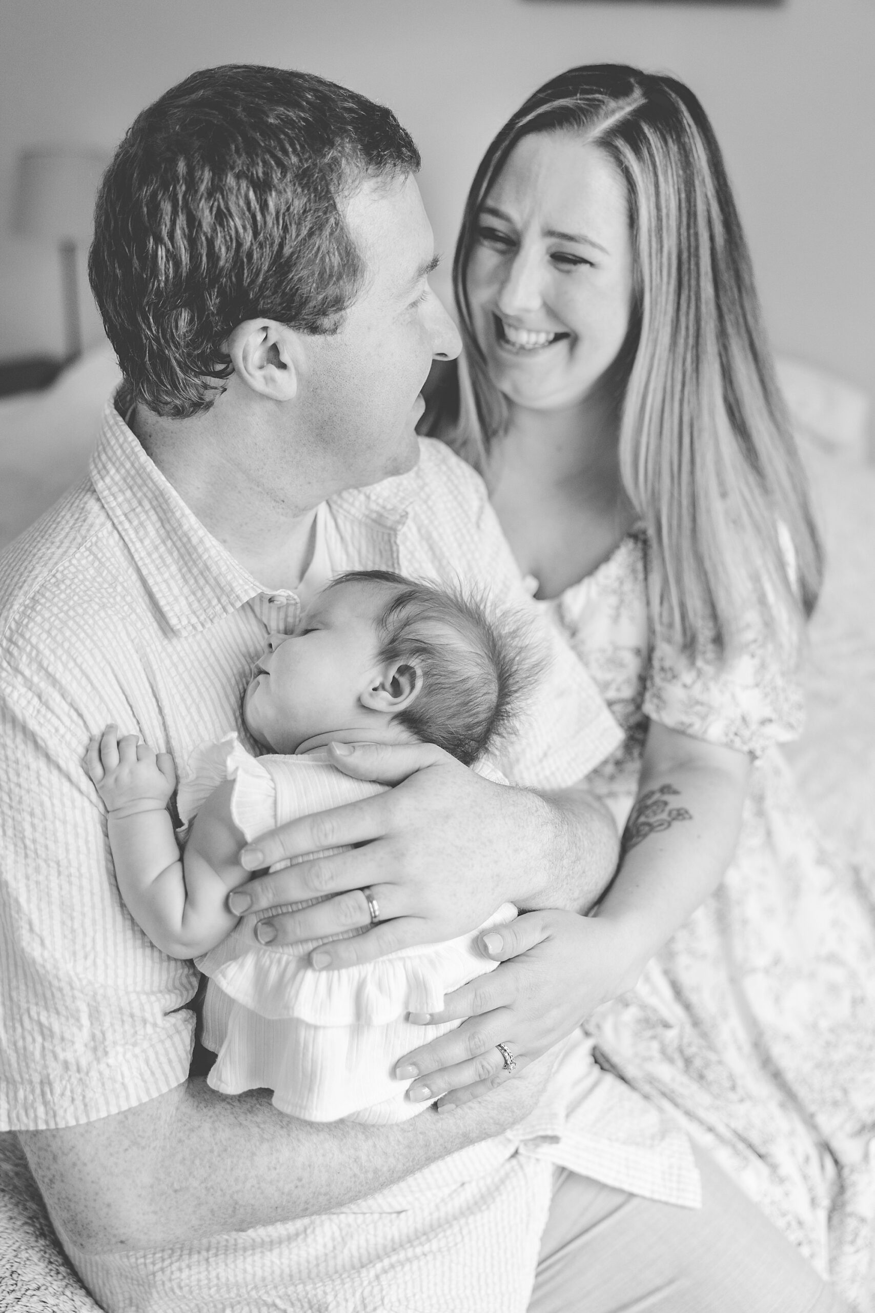 family of three smiles on bed during newborn photos in Maryland