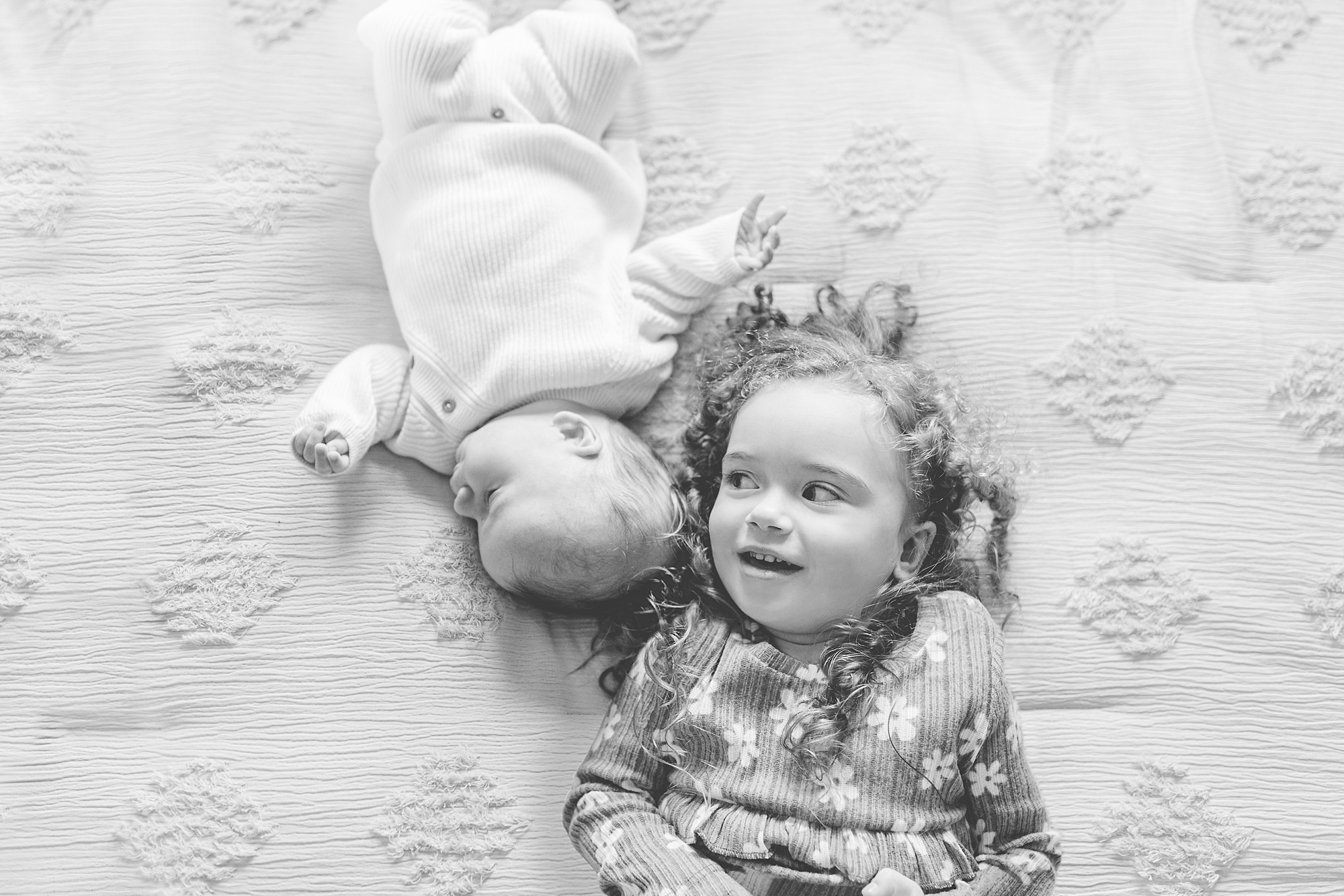 toddler and baby sister lay on bed touching heads during Maryland newborn lifestyle session