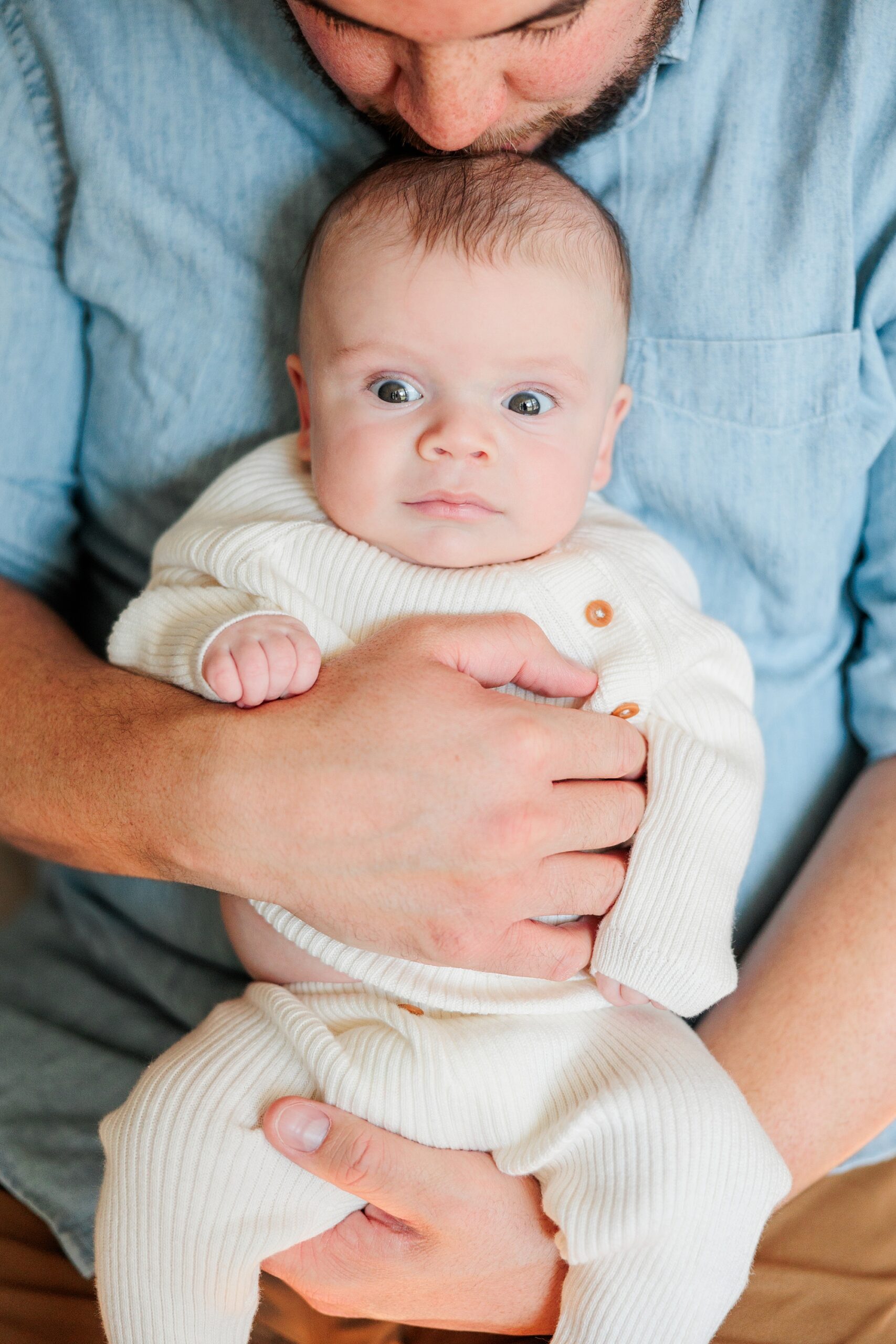 baby sits in dad's lap during newborn photos at home