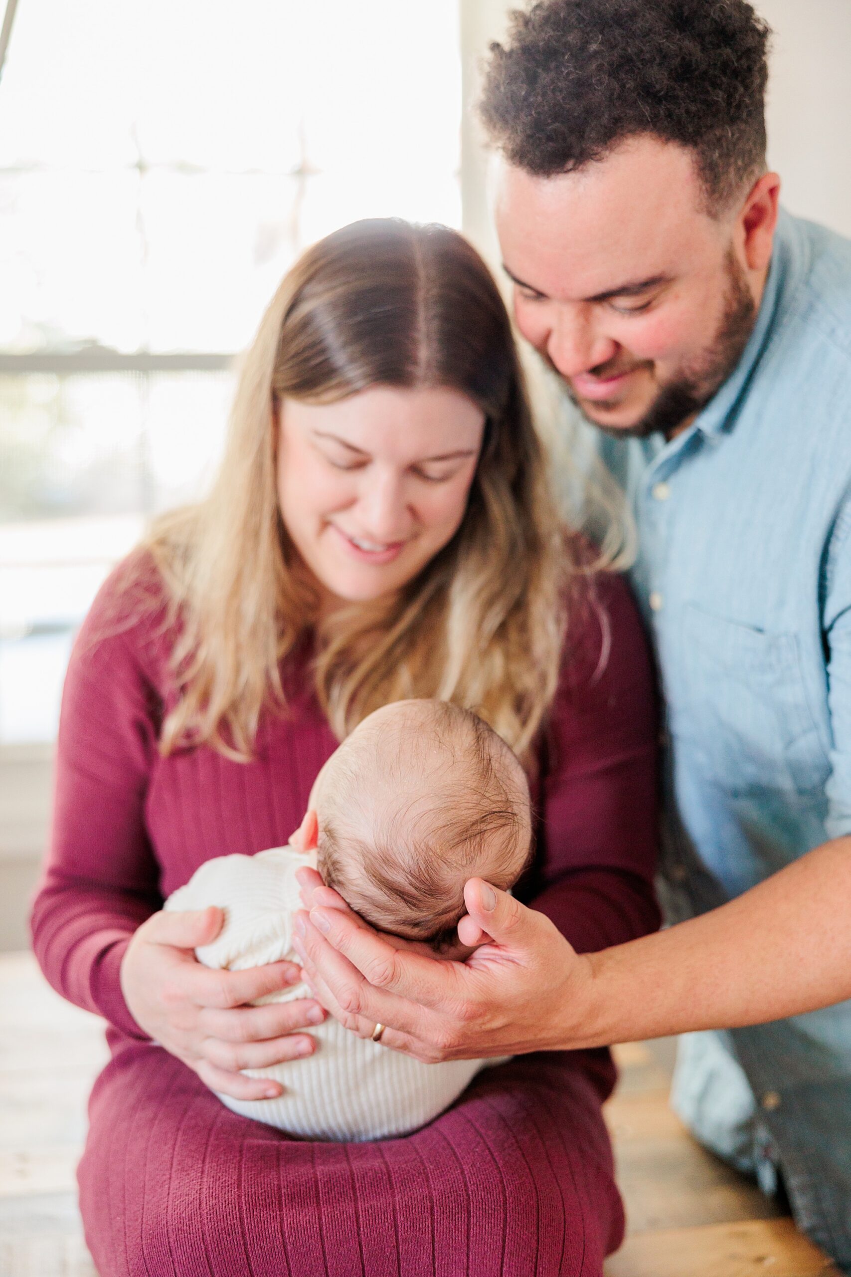 parents smile down at new baby girl in mom's hands during newborn photos at home