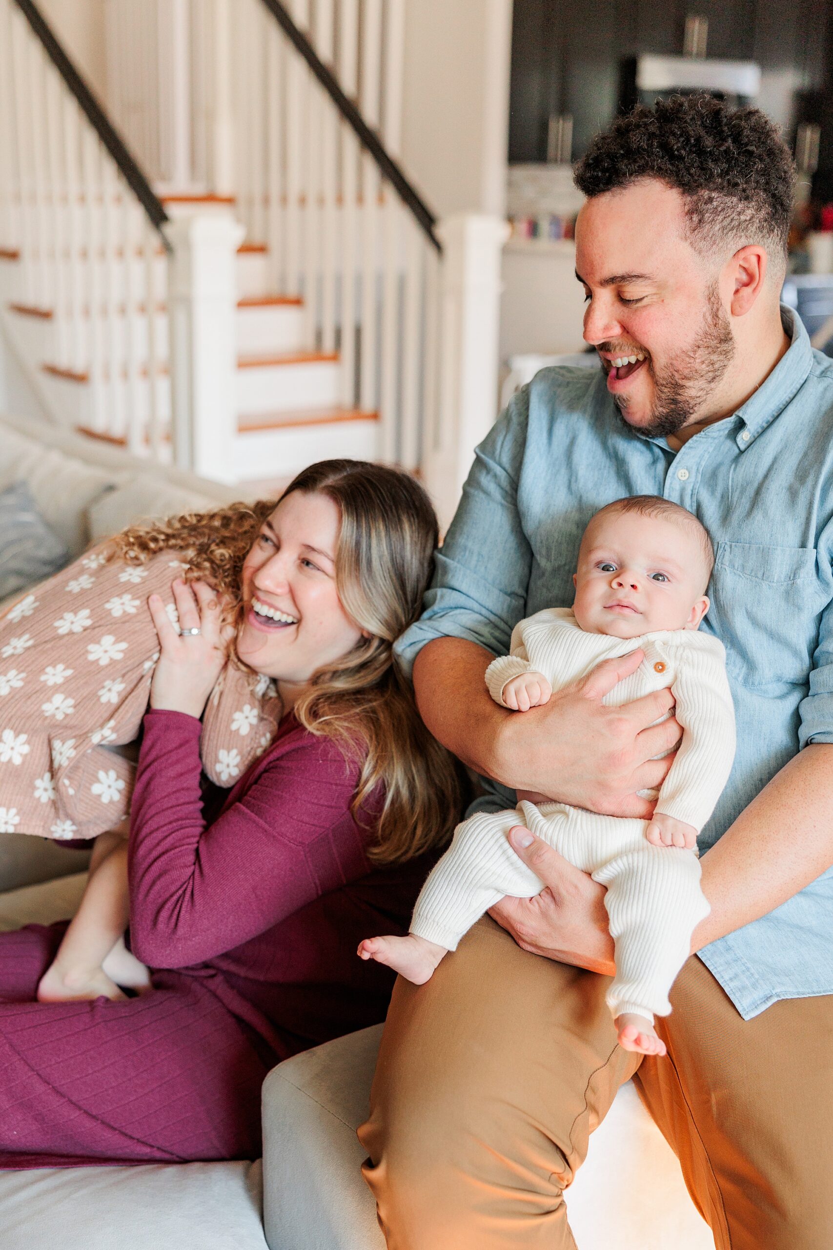 parents laugh playing with toddler and baby during newborn photos at home