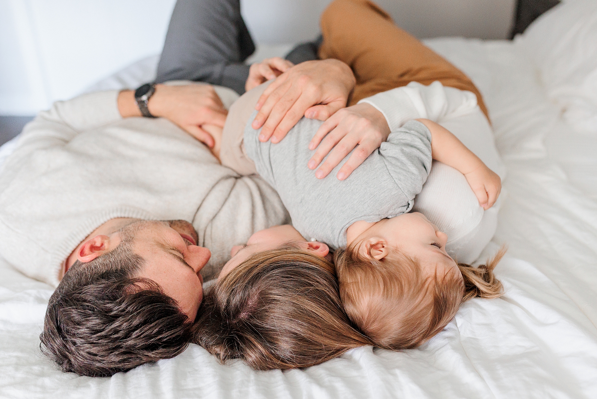 parents snuggle with son on bed during family photos at home 