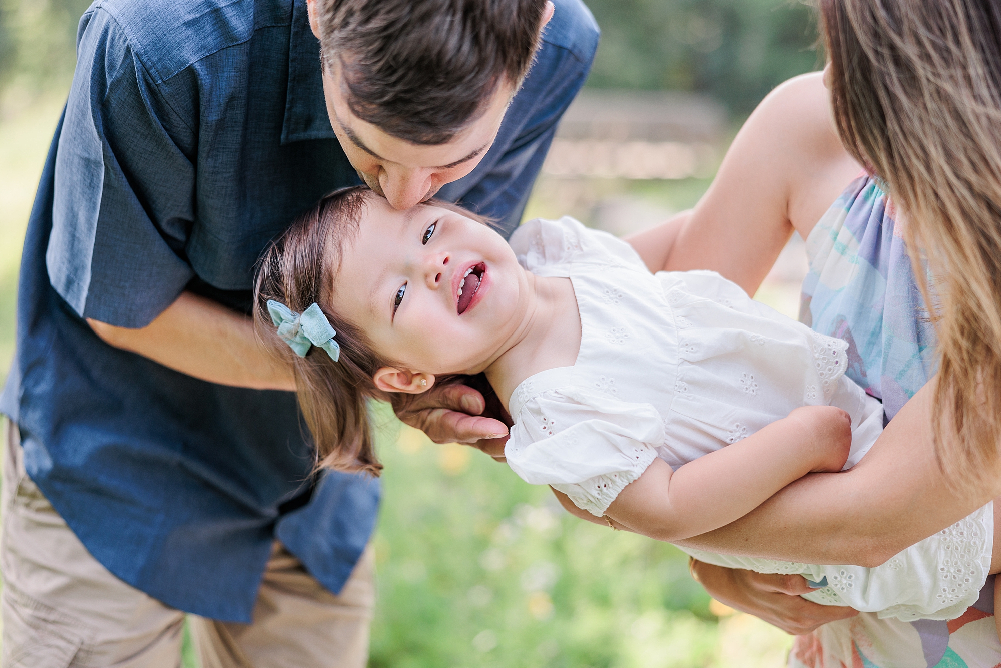 dad leans to kiss daughter on mom's hip playing during family photos 