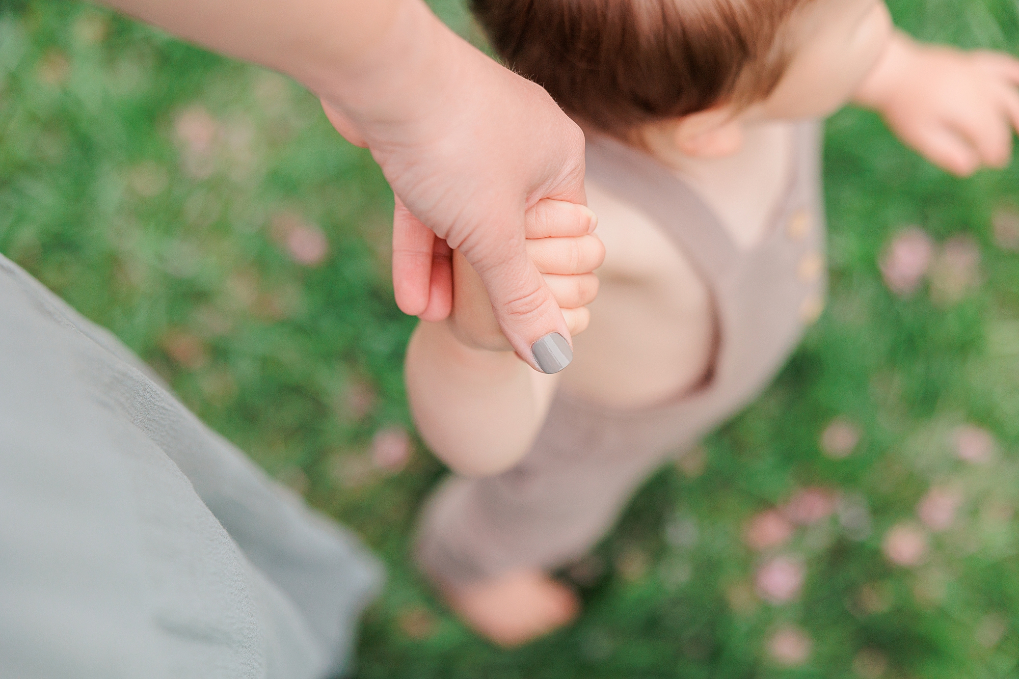 mother holds hand of young son walking through grass