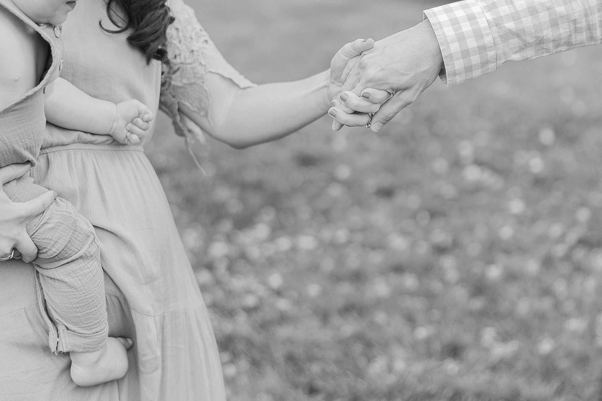 man holds woman's hand leading her across lawn as she carries child