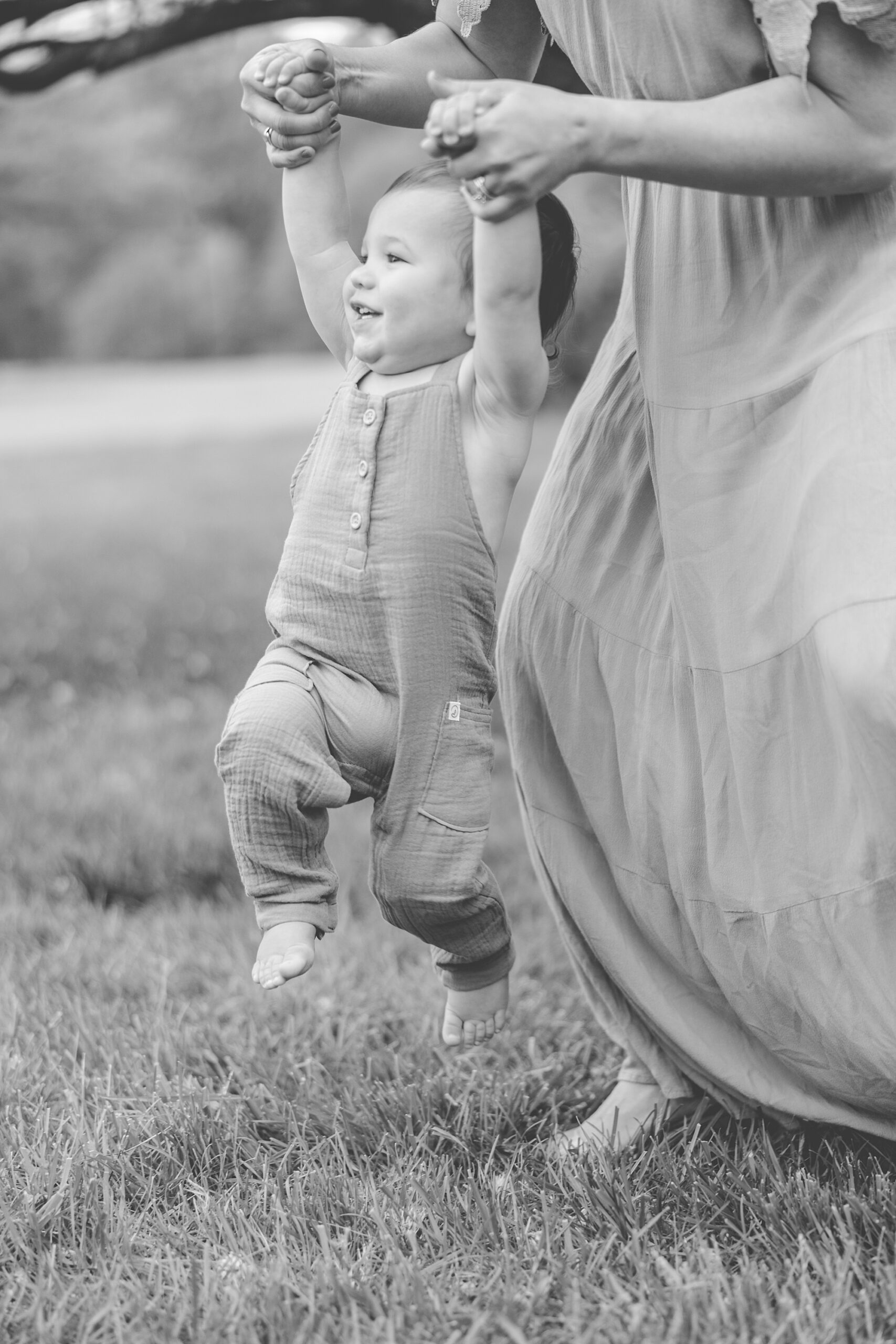 mom swings toddler walking through grass