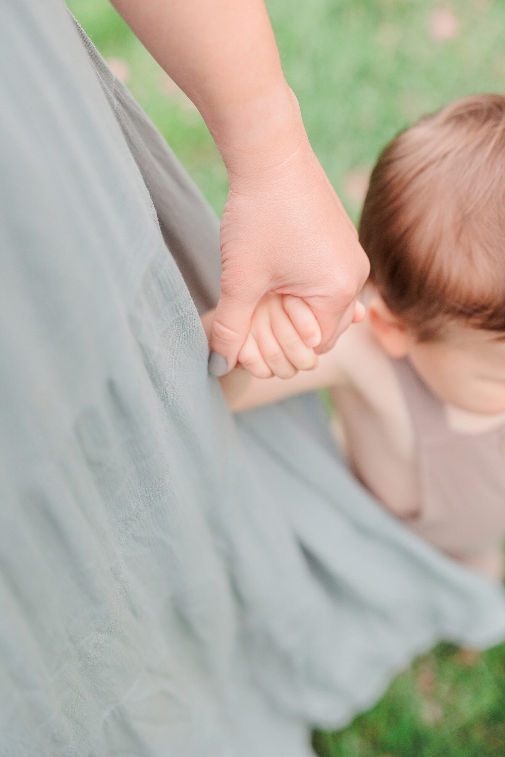 mom holds son's hand while he toddles on grass