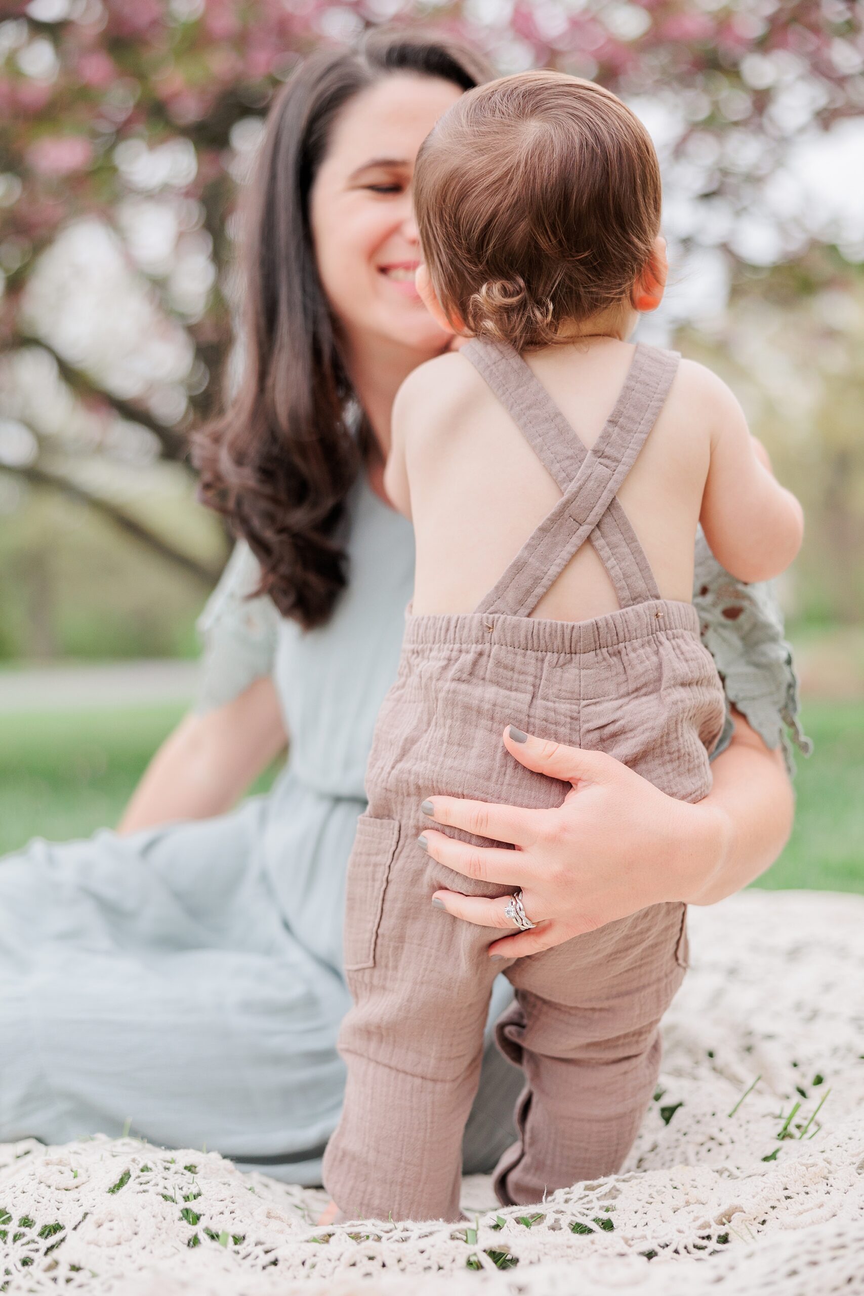 mom holds baby around hips during family photos on blanket