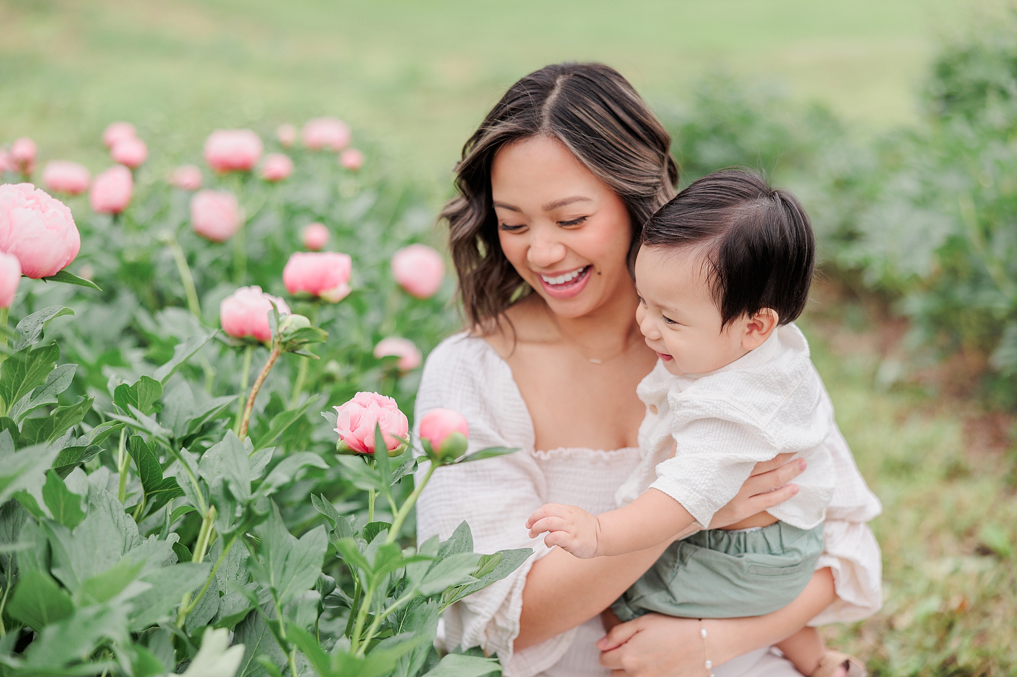 mom laughs holding son to reach pink peonies at Castlebridge Farm