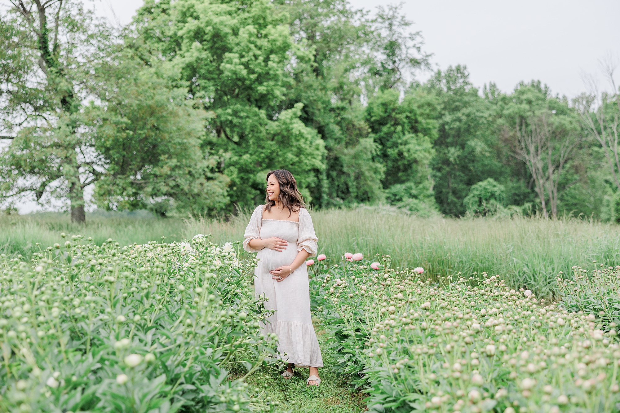 mom stands in field of wildflowers holding baby bump