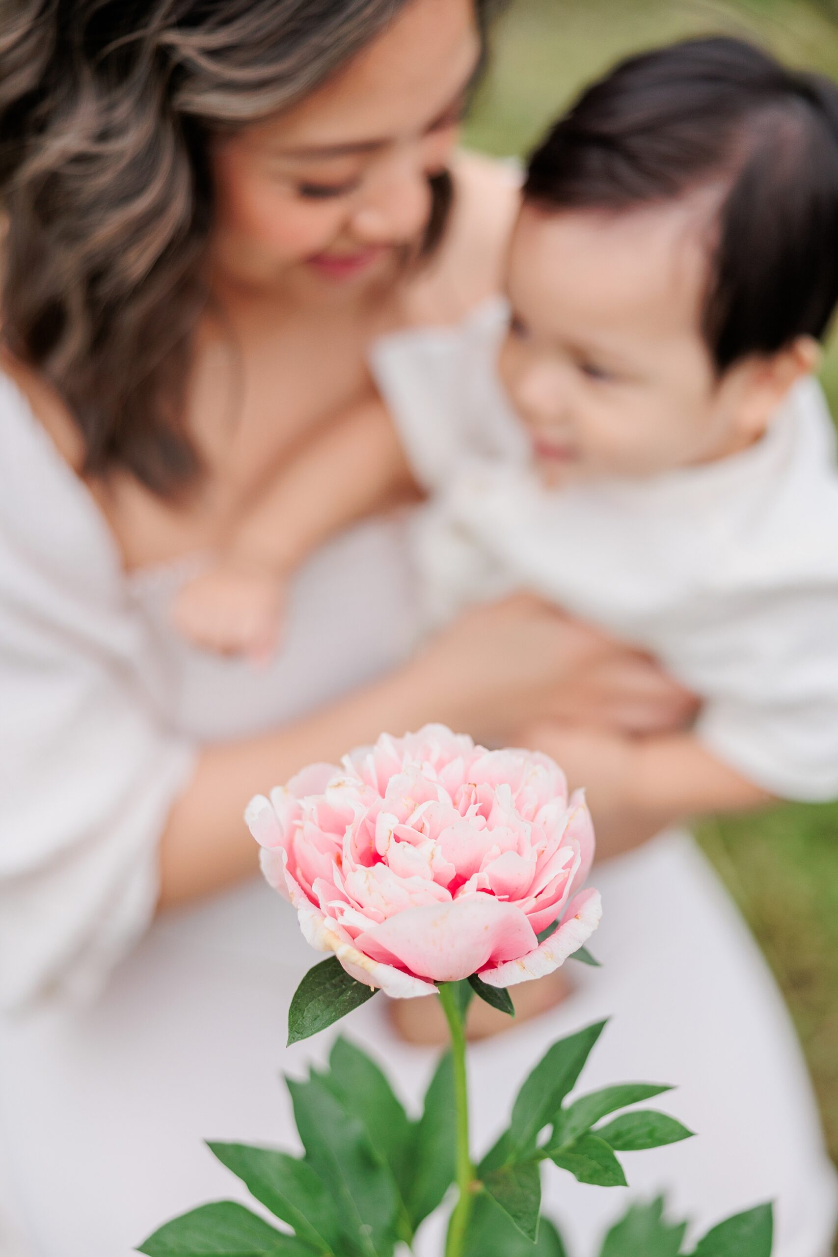 pink peony in front of mom and son snuggling