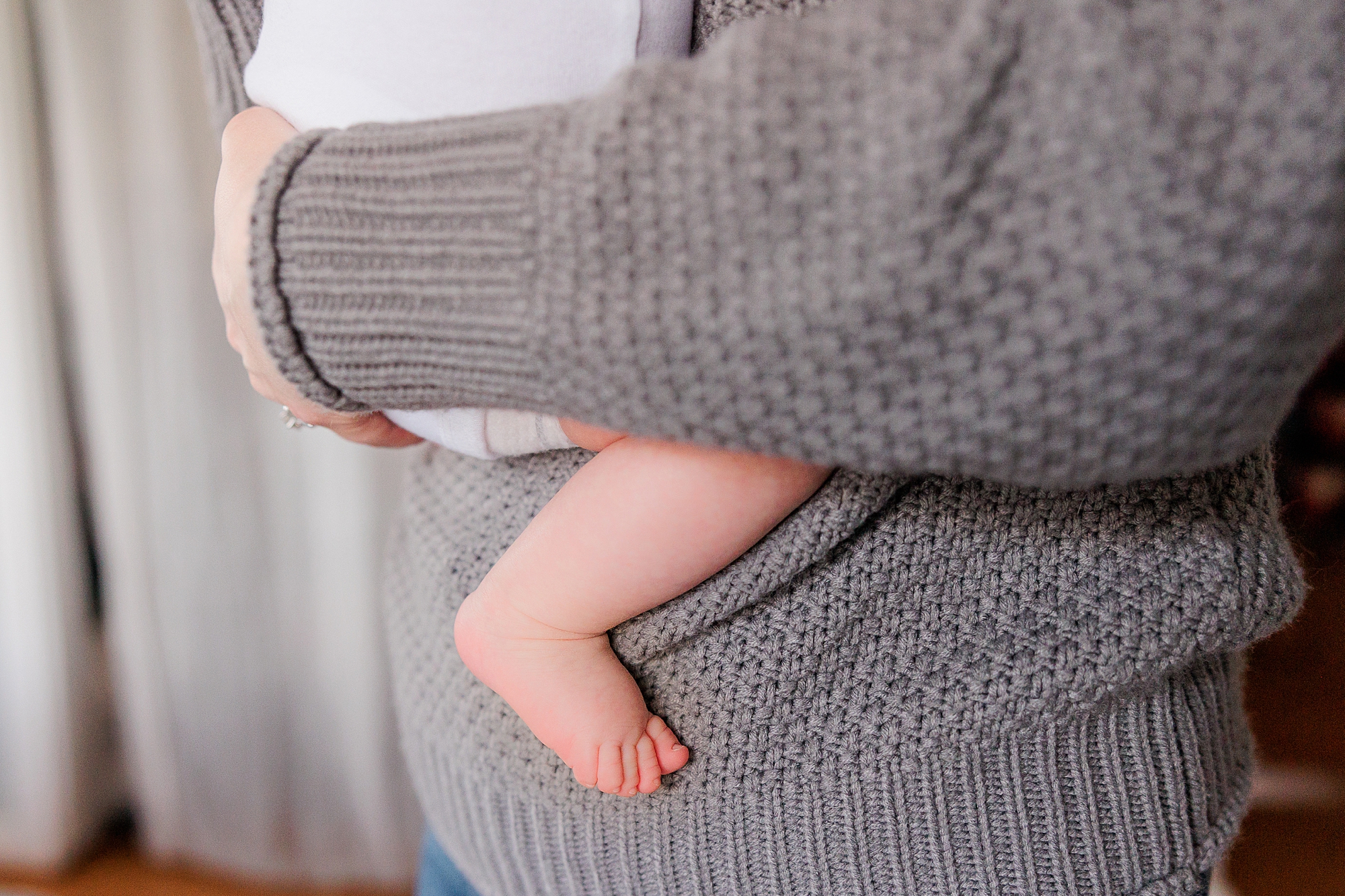 woman in grey sweater holds baby to her chest 