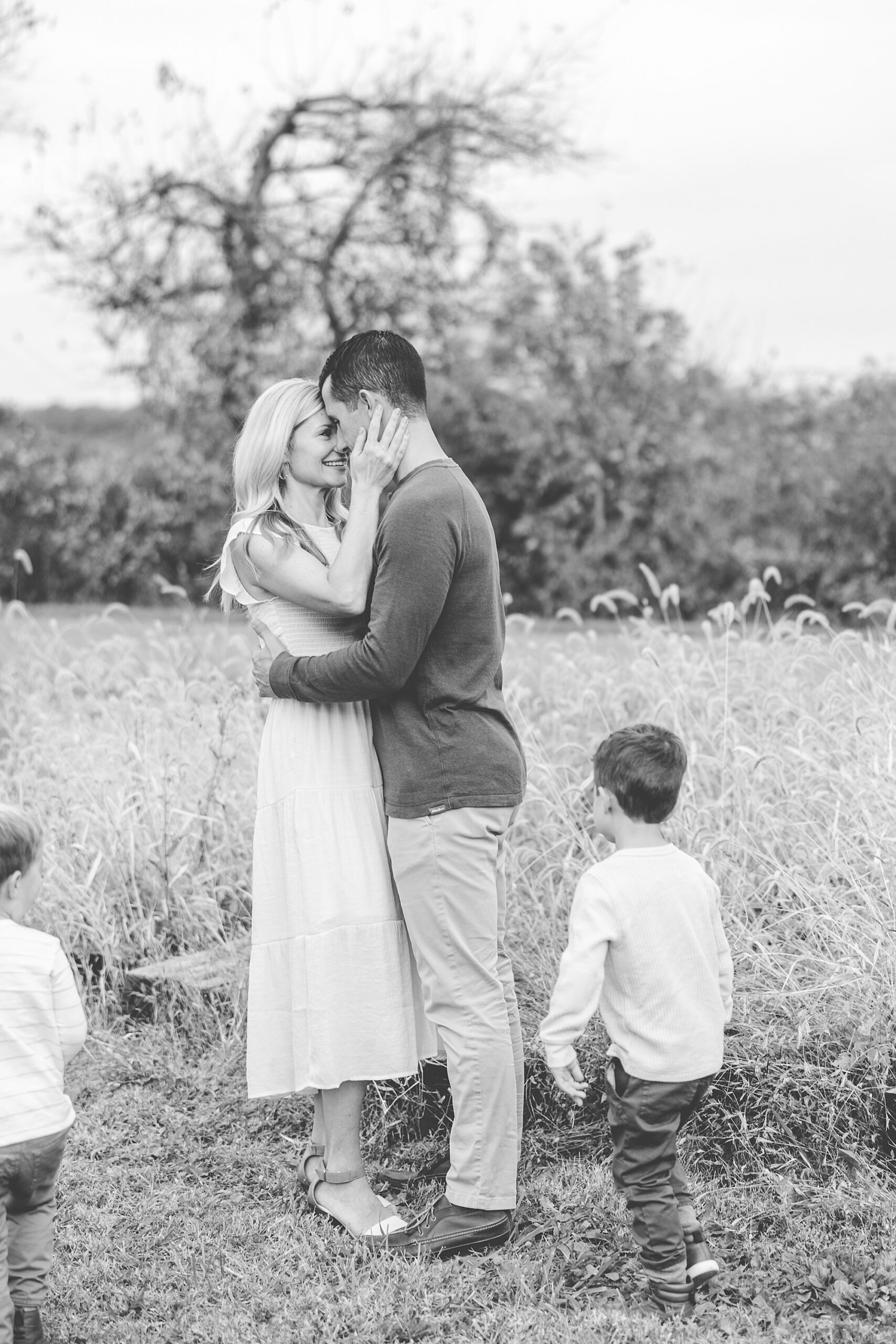 couple hugs while children run around them in a field