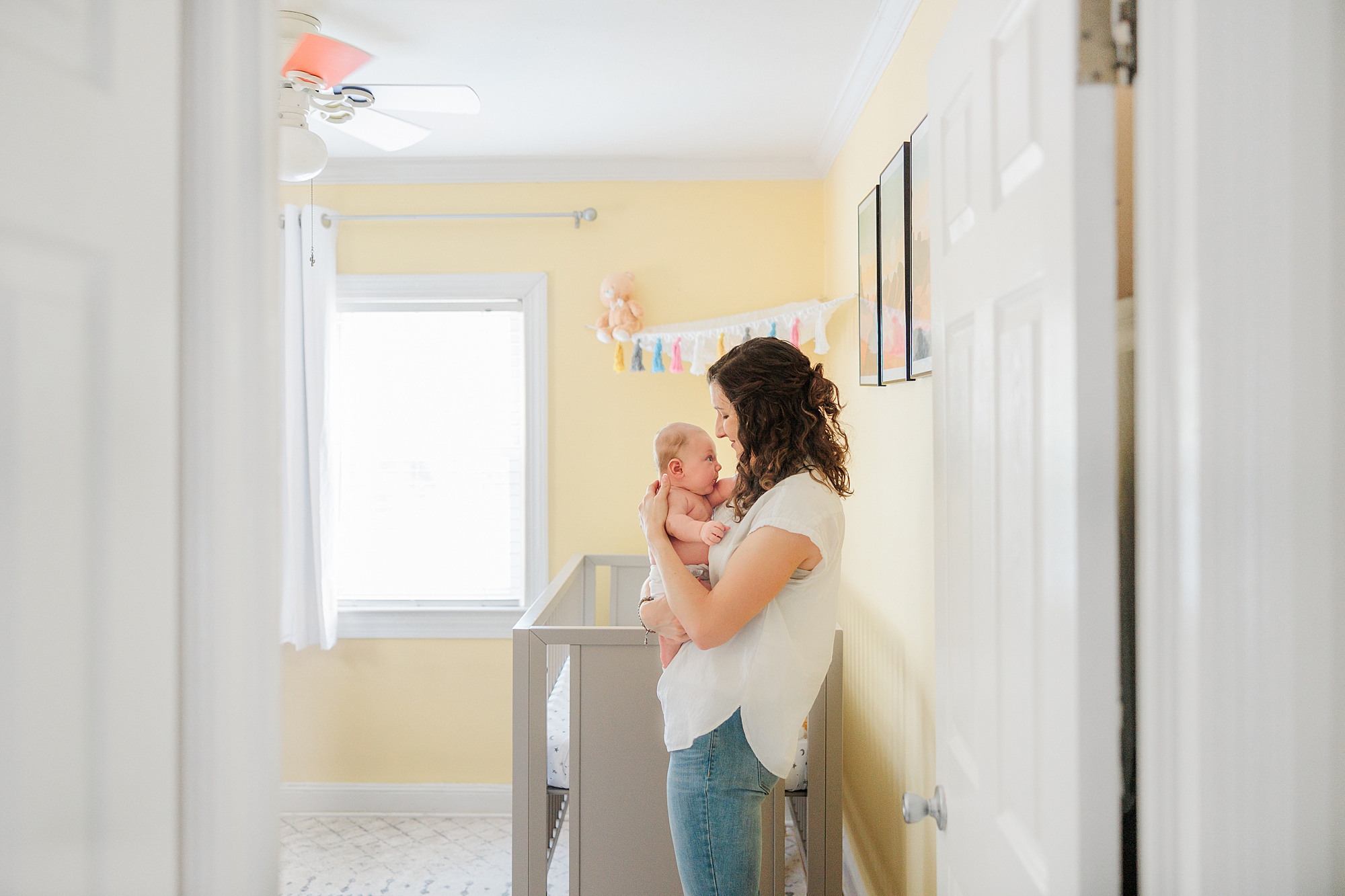 mom holds baby boy in doorway of his nursery during newborn lifestyle photography session