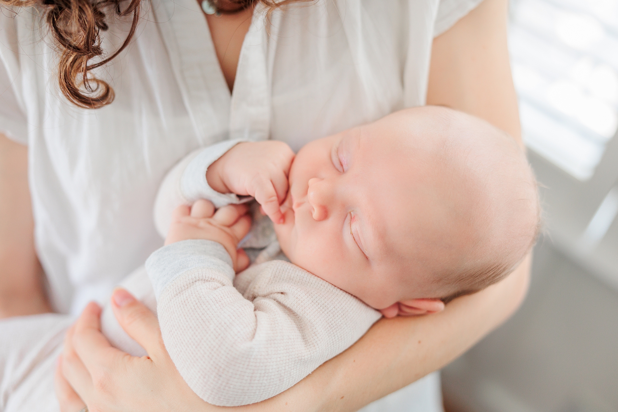 mom holds son wrapped in white onesie during newborn photos at home