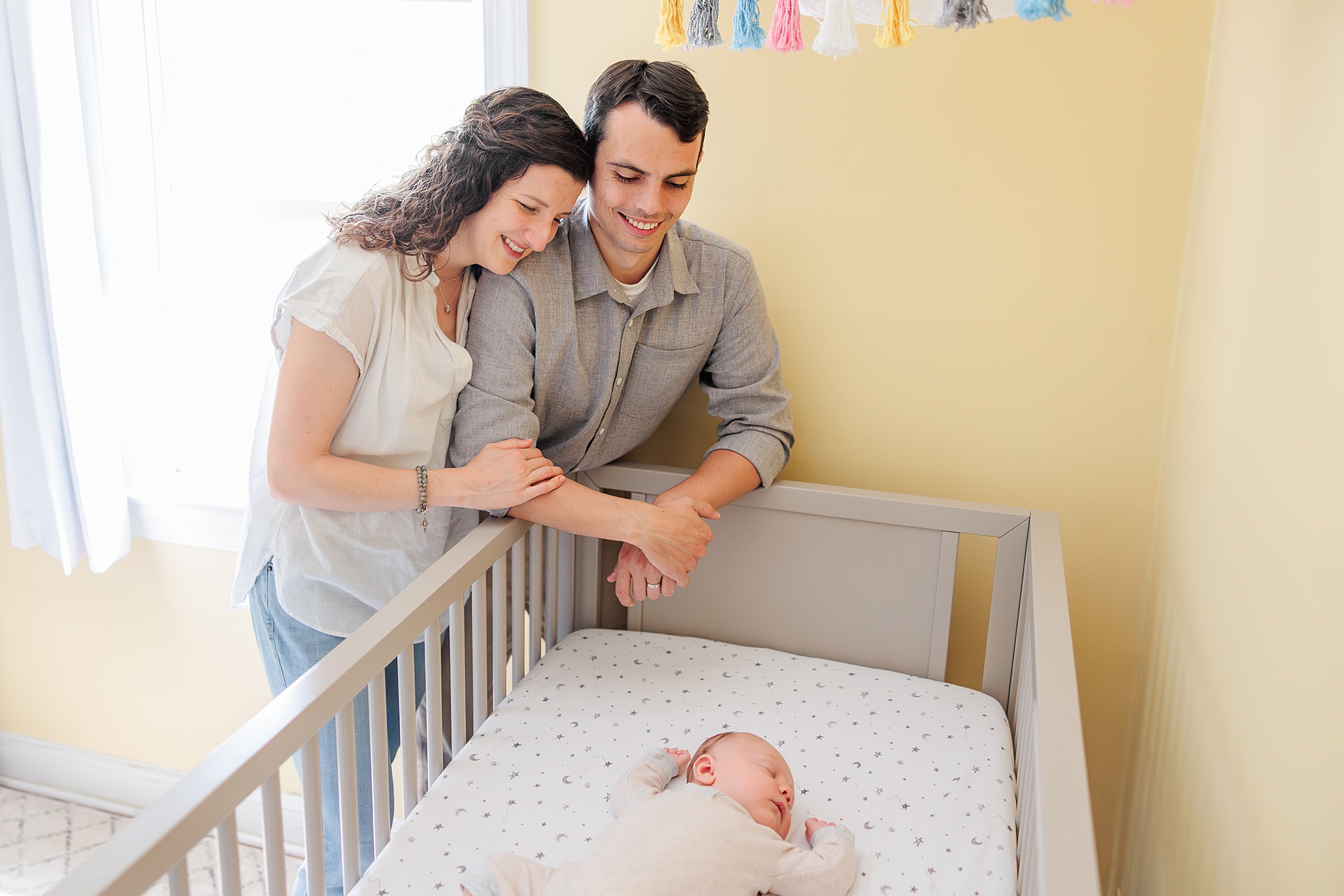 parents hug by crib during newborn lifestyle photography session in Maryland home