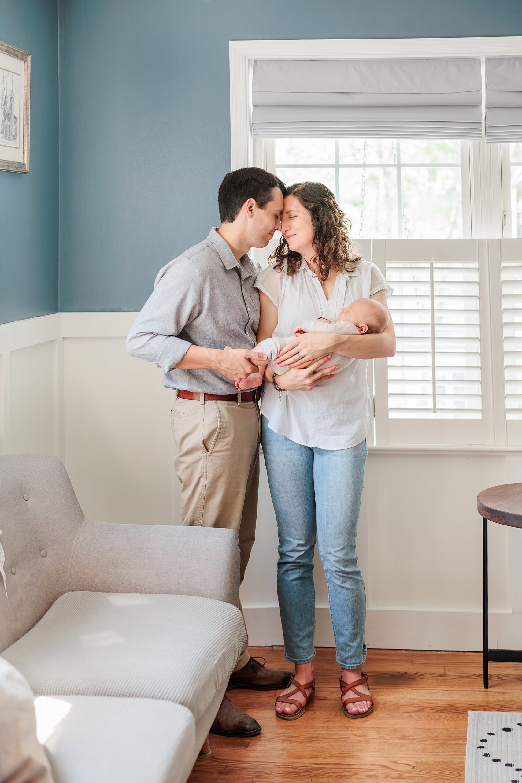 married couple hugs baby in corner of nursery during newborn lifestyle photography session