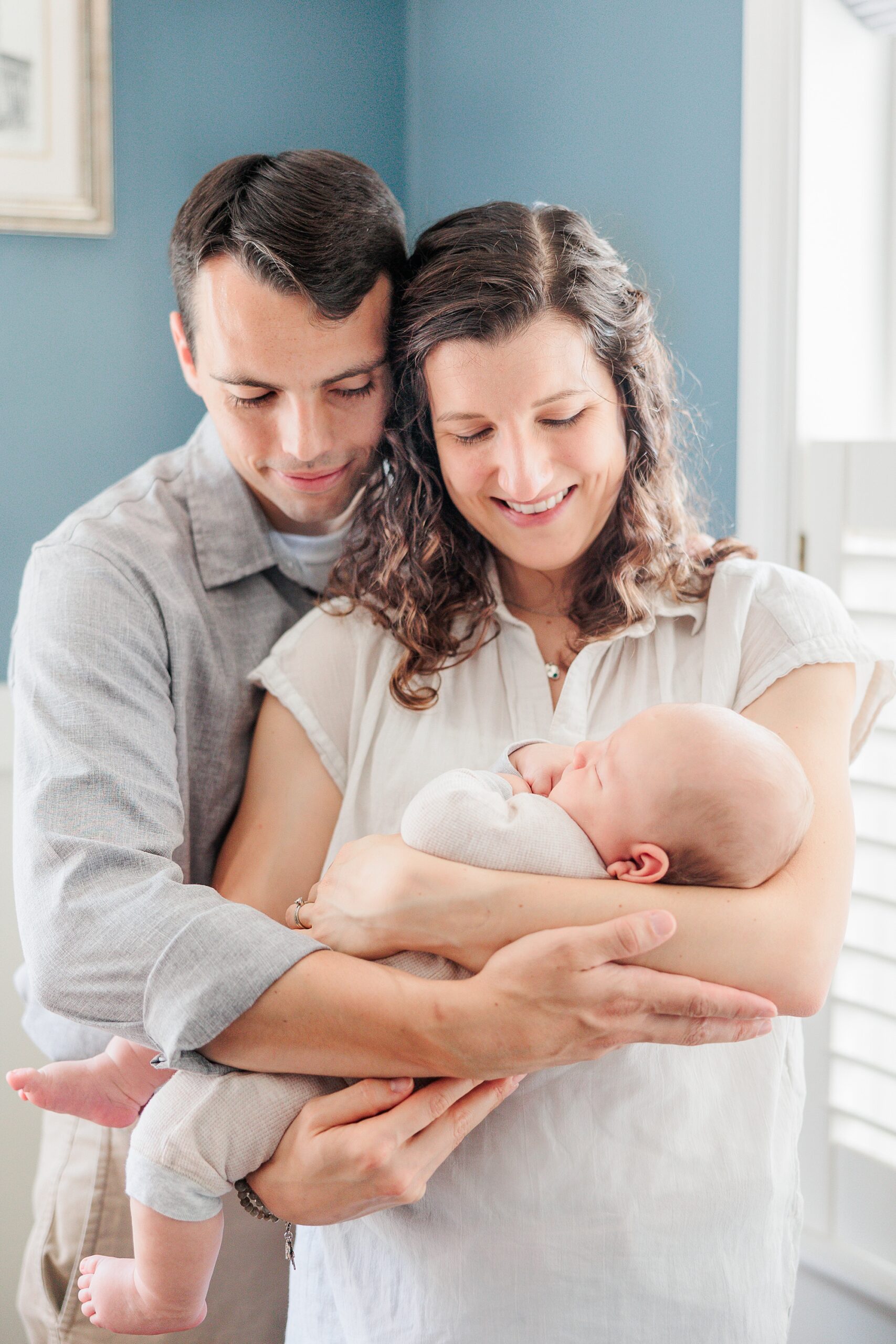 parents hug holding newborn son in front of them during newborn lifestyle photography session at home 