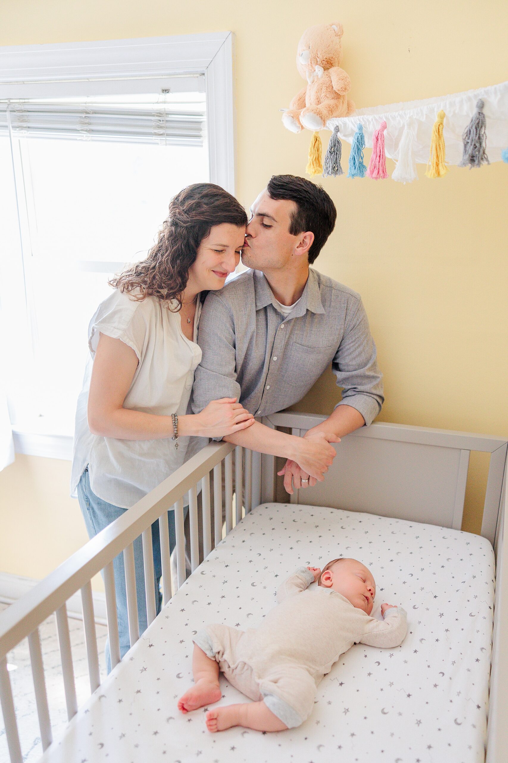 parents kiss while standing over newborn baby in crib