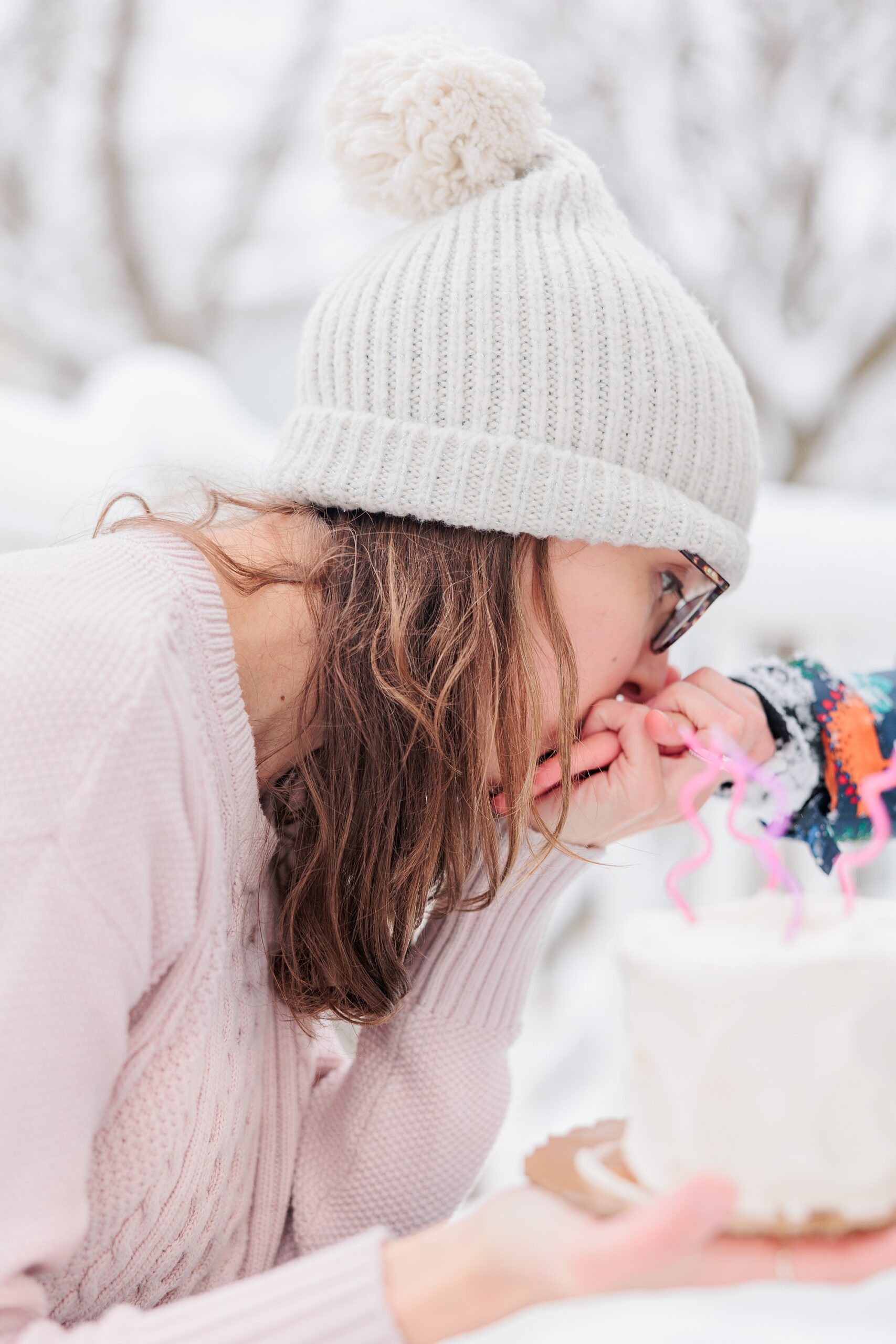 woman in pink sweater holds birthday cake and kisses son's hand