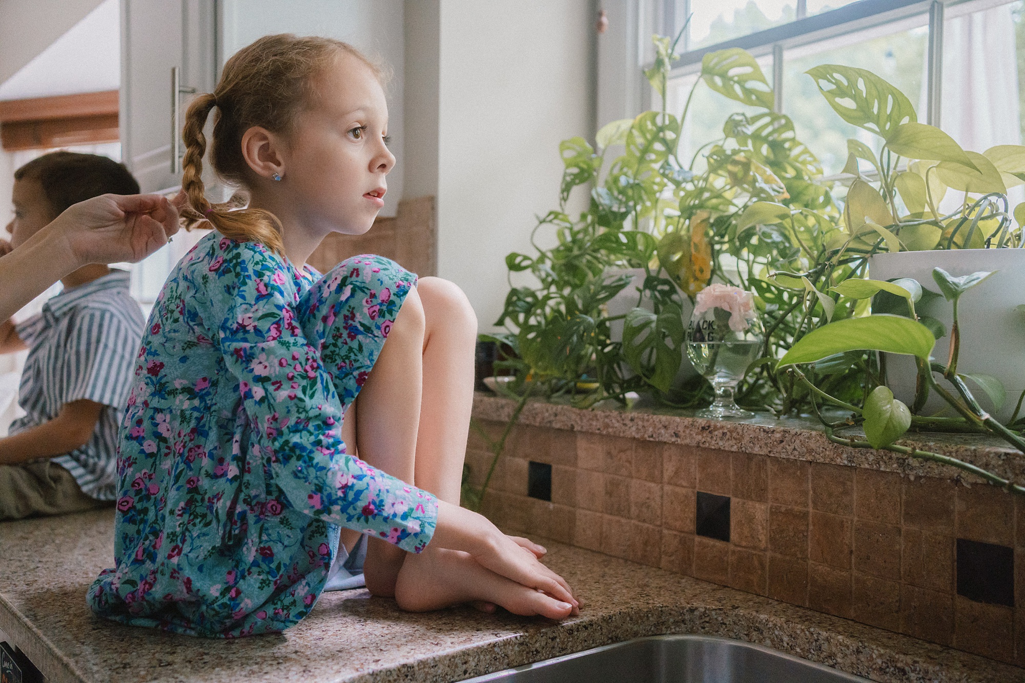 girl sits on sink looking out the window in the kitchen 