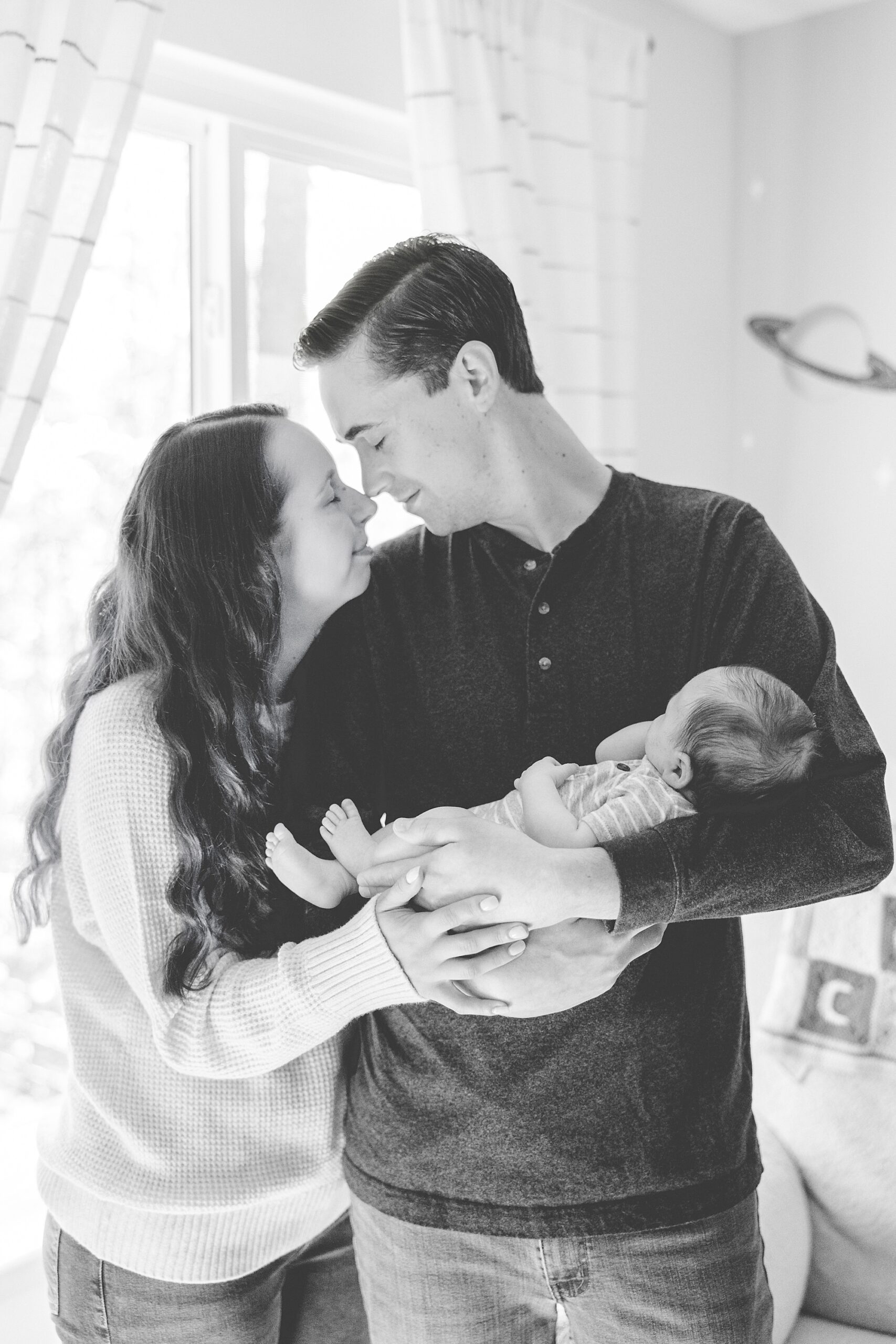 couple smiles leaning together while dad holds newborn son 