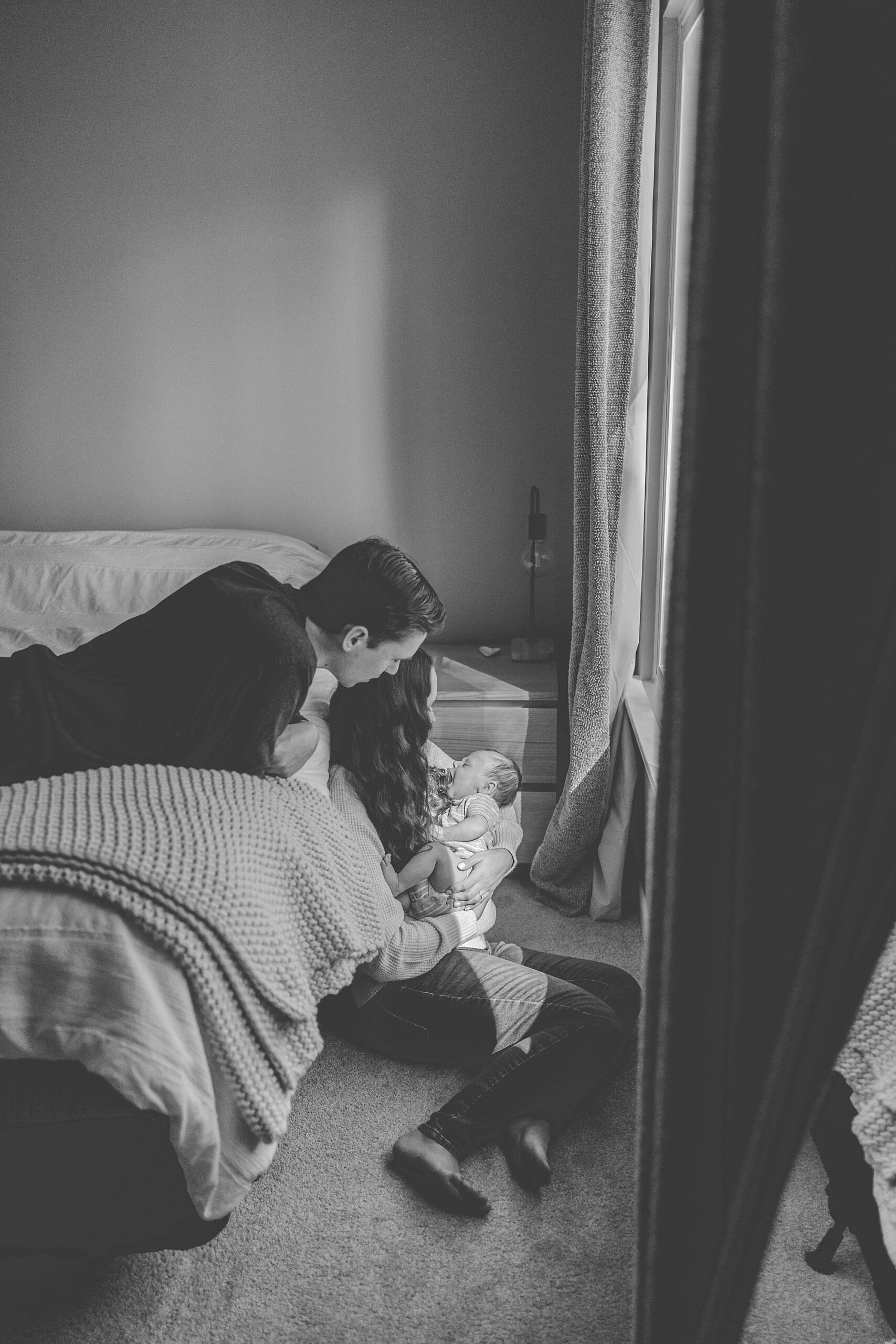 dad looks over mom's shoulder laying on bed in Baltimore home