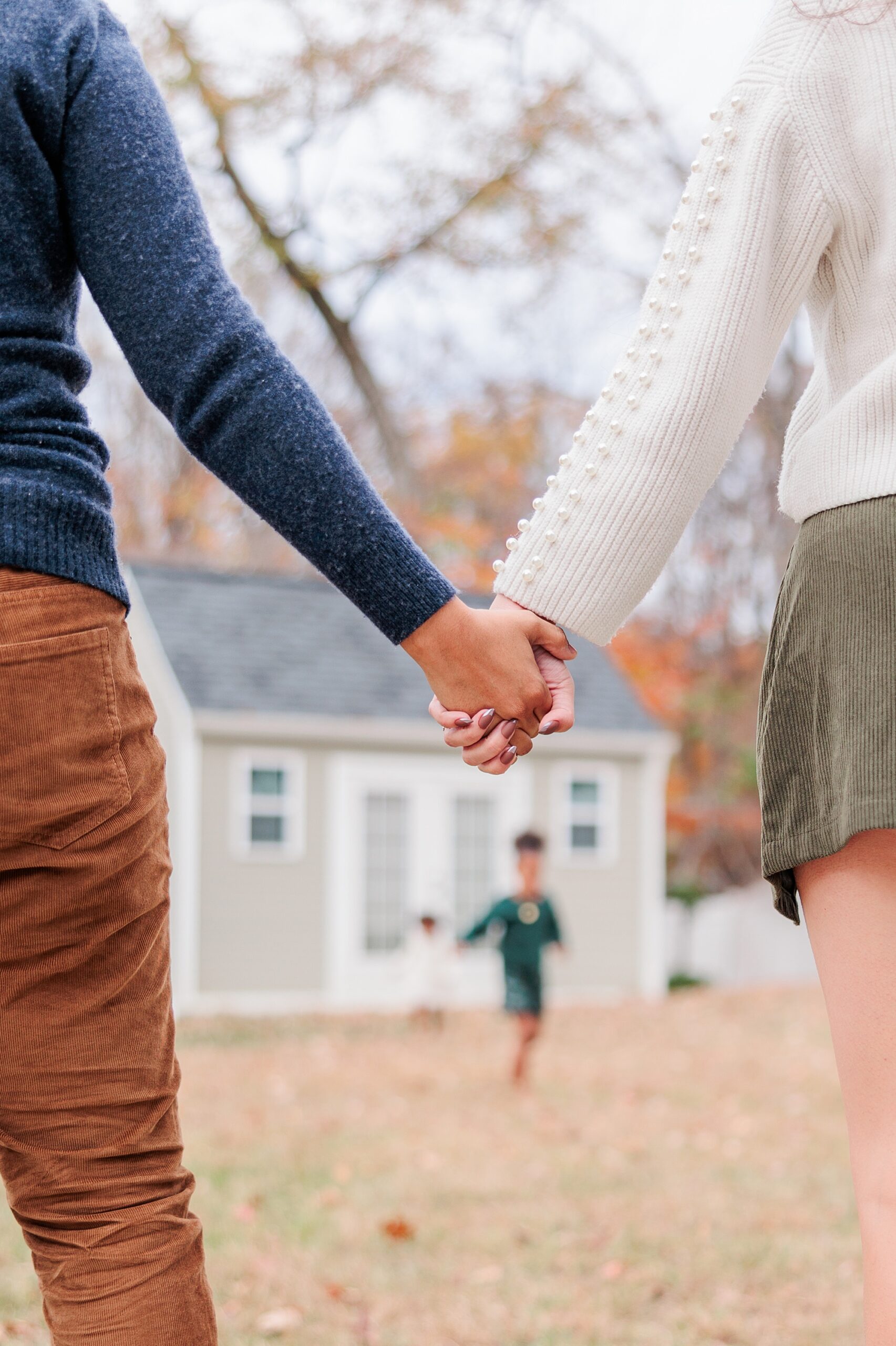 parents hold hands while daughter runs in yard in front of them