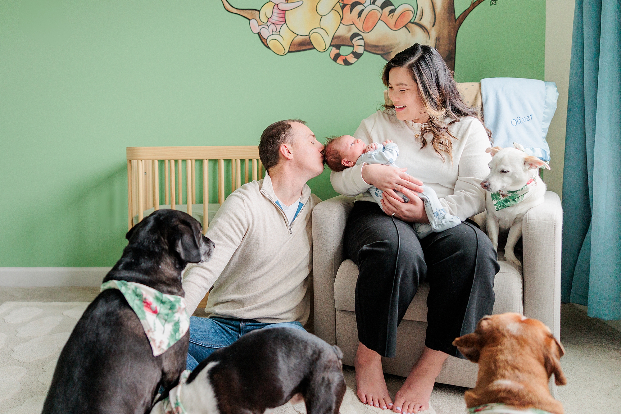 dad leans to kiss baby's head while petting dog during newborn session with Baltimore photographer