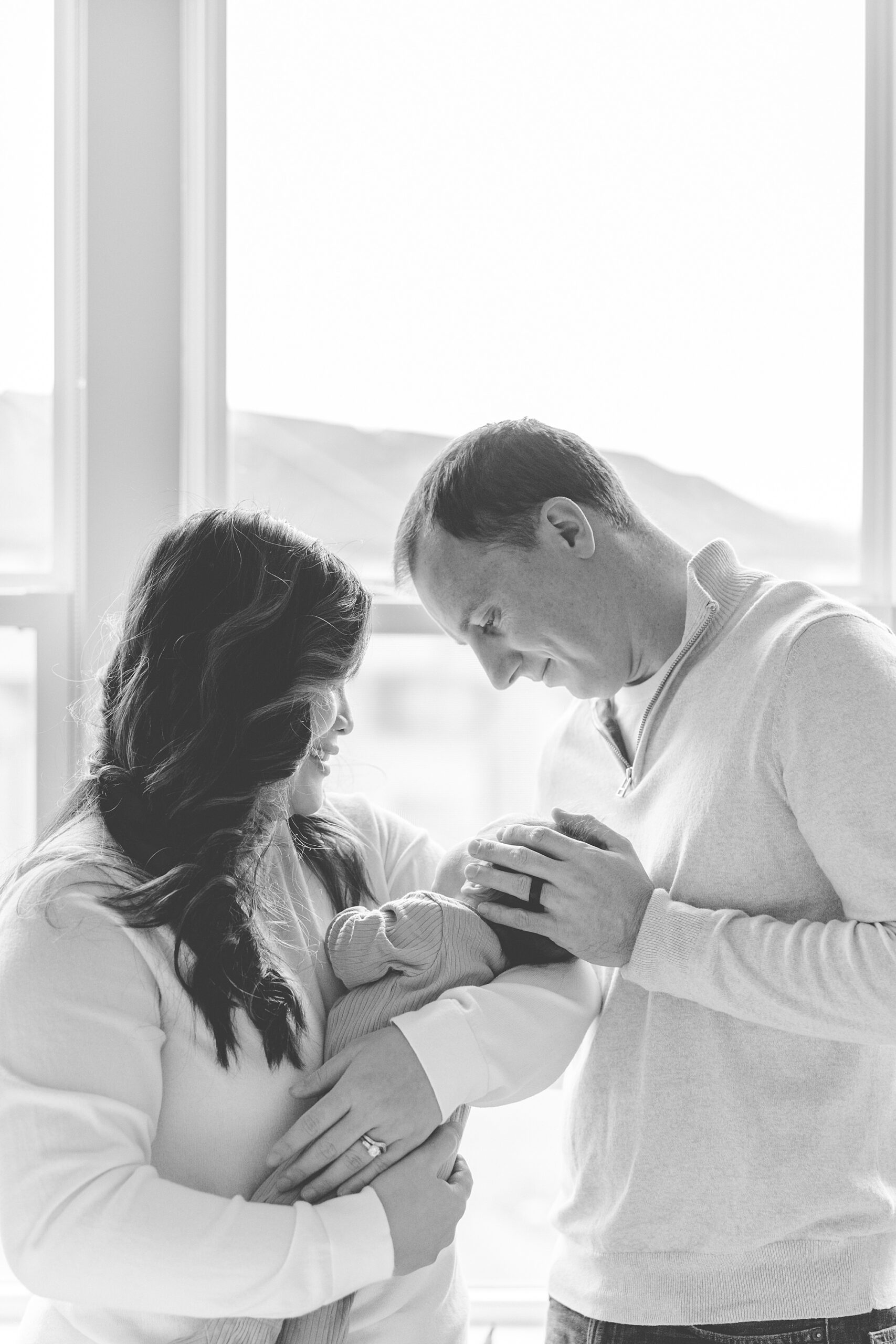 mom and dad look at newborn in front of window in Baltimore home