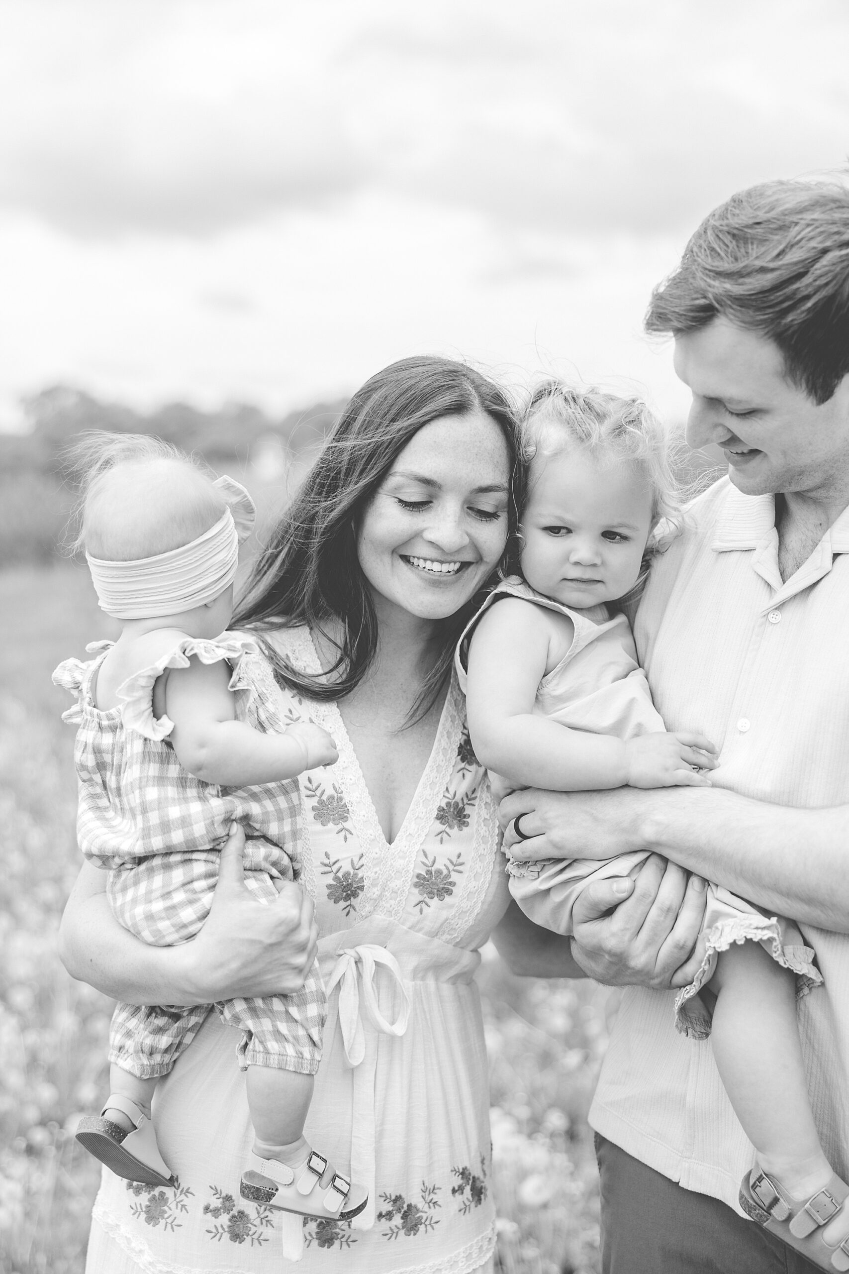 parents smile with toddler daughters on hips during Baltimore lifestyle family session on farm