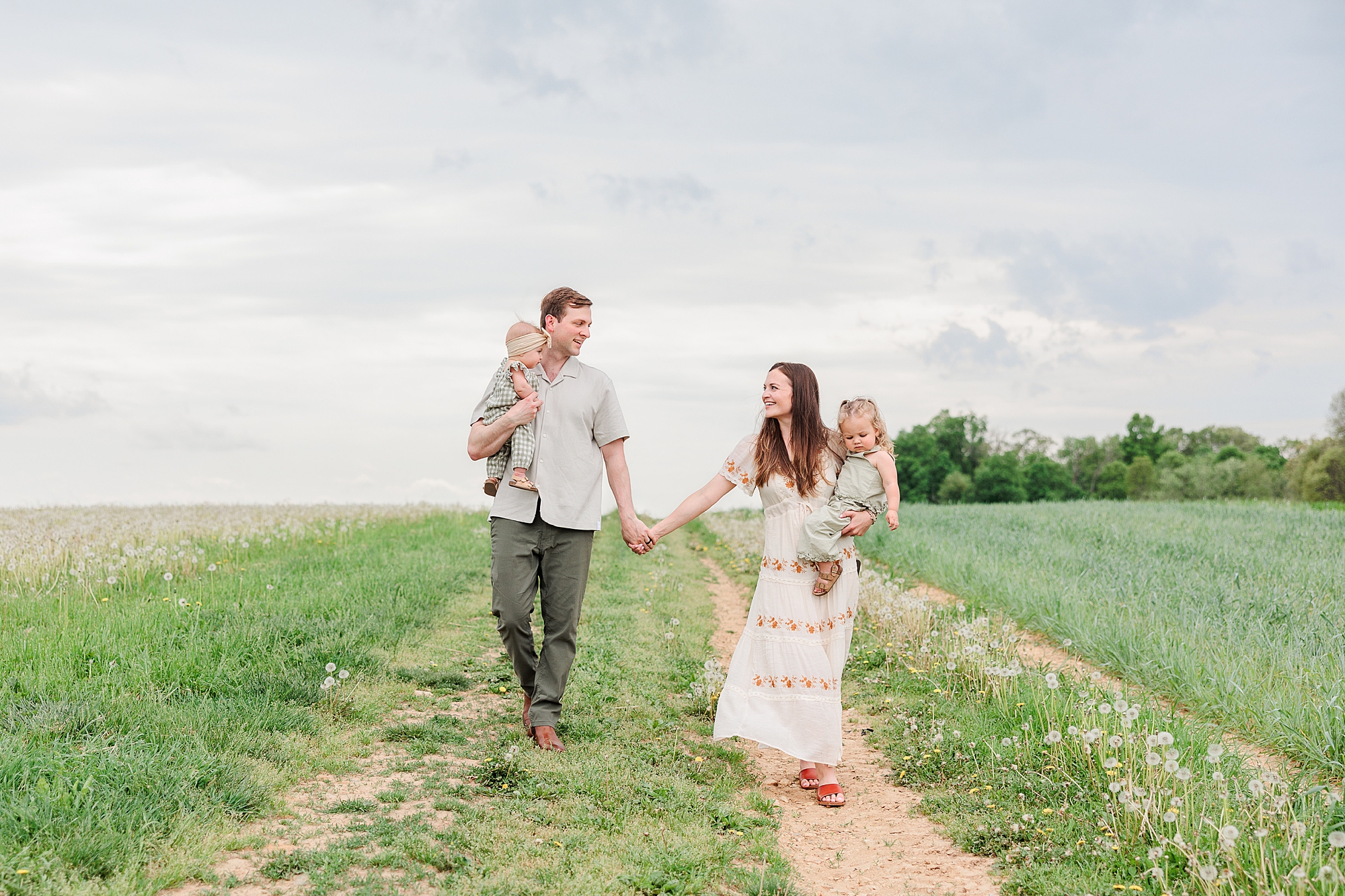 couple holds hands walking thorough field on farm