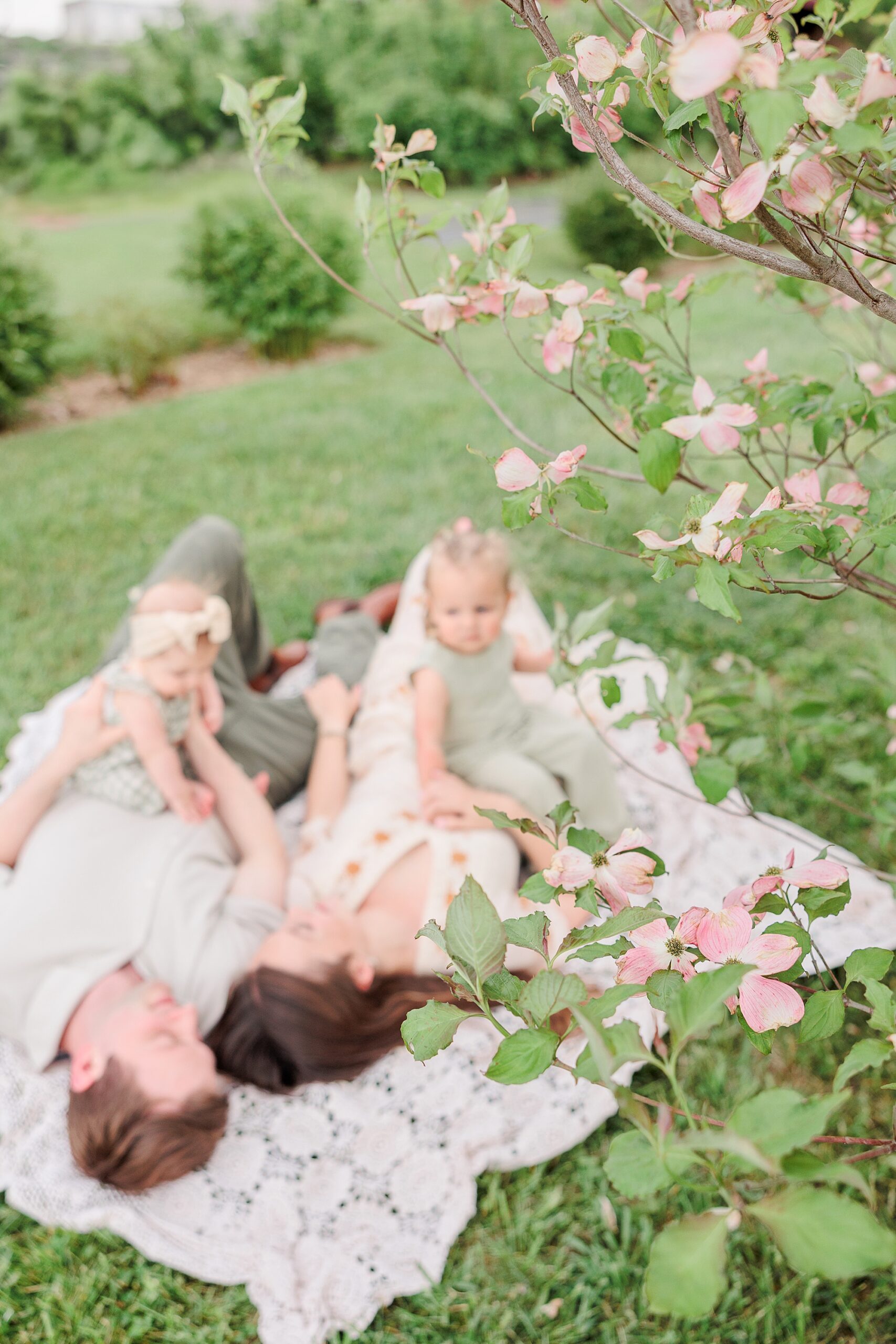 parents lay on blanket playing with daughters during Baltimore lifestyle family session on farm
