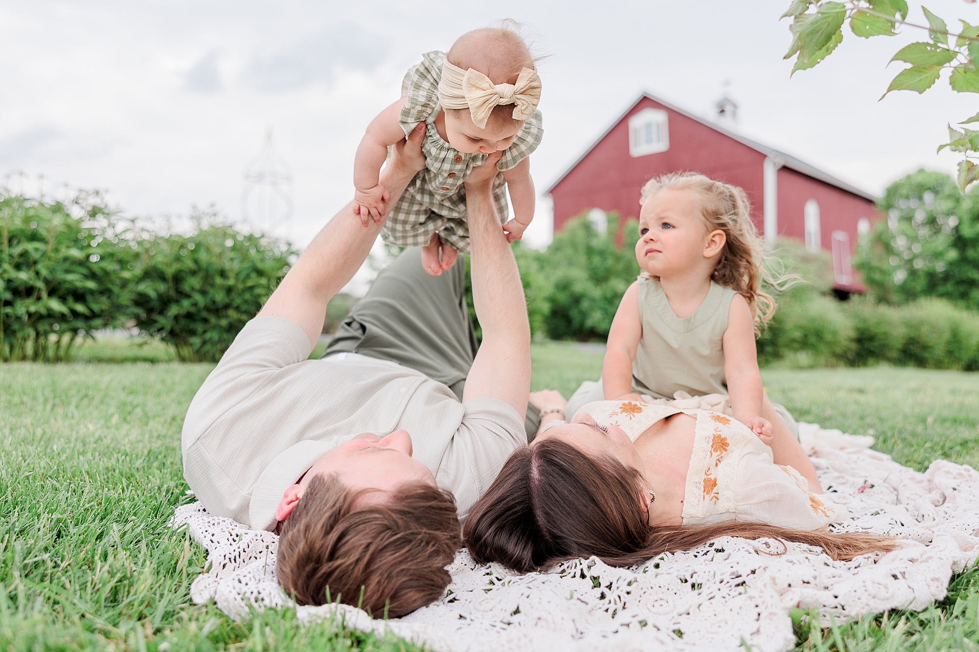 parents lay on blanket playing with daughters during Baltimore lifestyle family session on farm